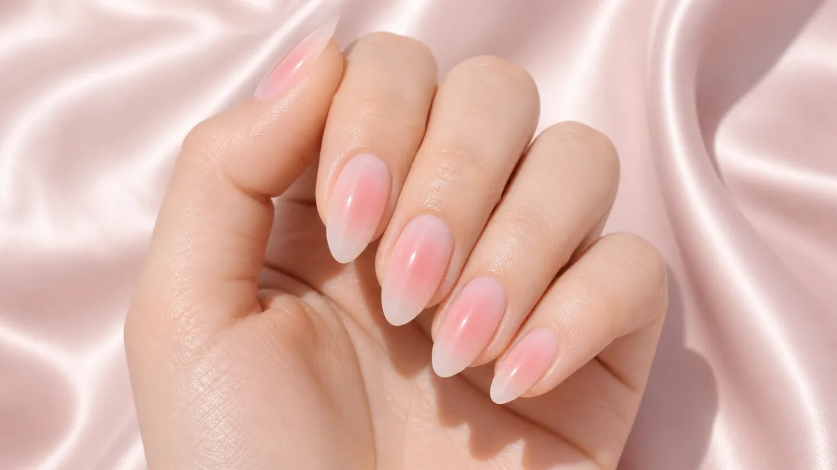 Close-up of almond nails with a soft blush aura airbrushed from the center of each nail, on fair skin resting on soft-pink silk