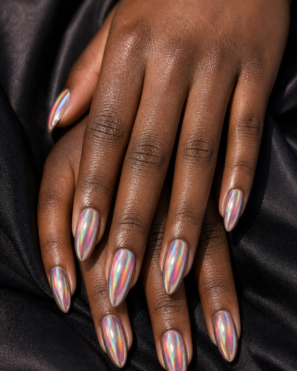 Macro of almond nails in a holographic chrome flickering rainbow colors in the light, on deep skin against dark fabric