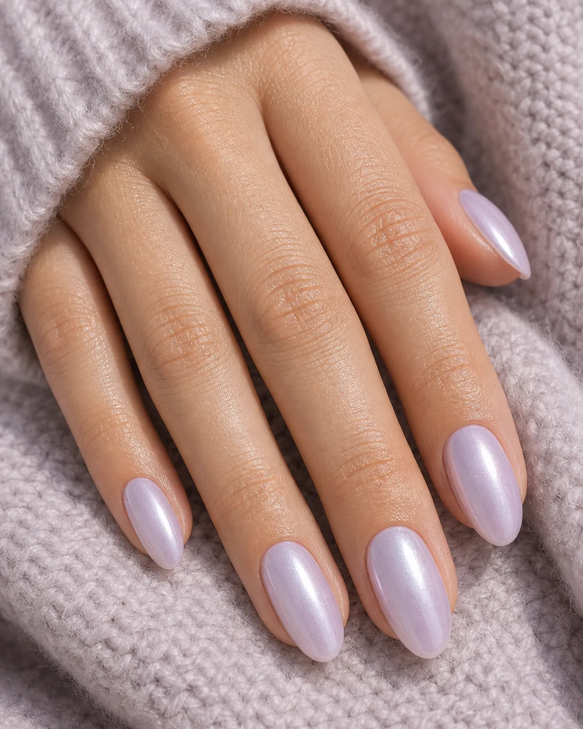 Close-up of medium oval nails in a pale lavender glazed donut finish with a cool pearl topper, on light-medium skin resting on a soft knit sleeve