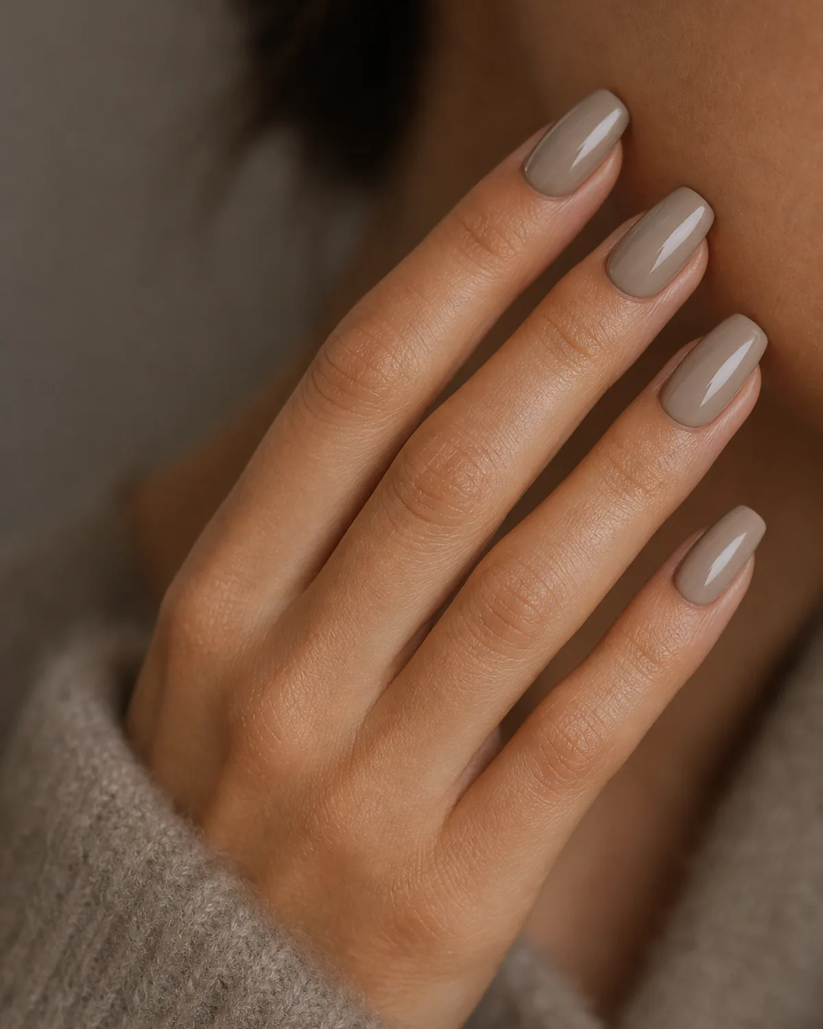 Close-up of medium coffin nails in wet-look glossy warm greige lacquer covering the entire nail surface like polished river stone, on medium skin against soft taupe wool