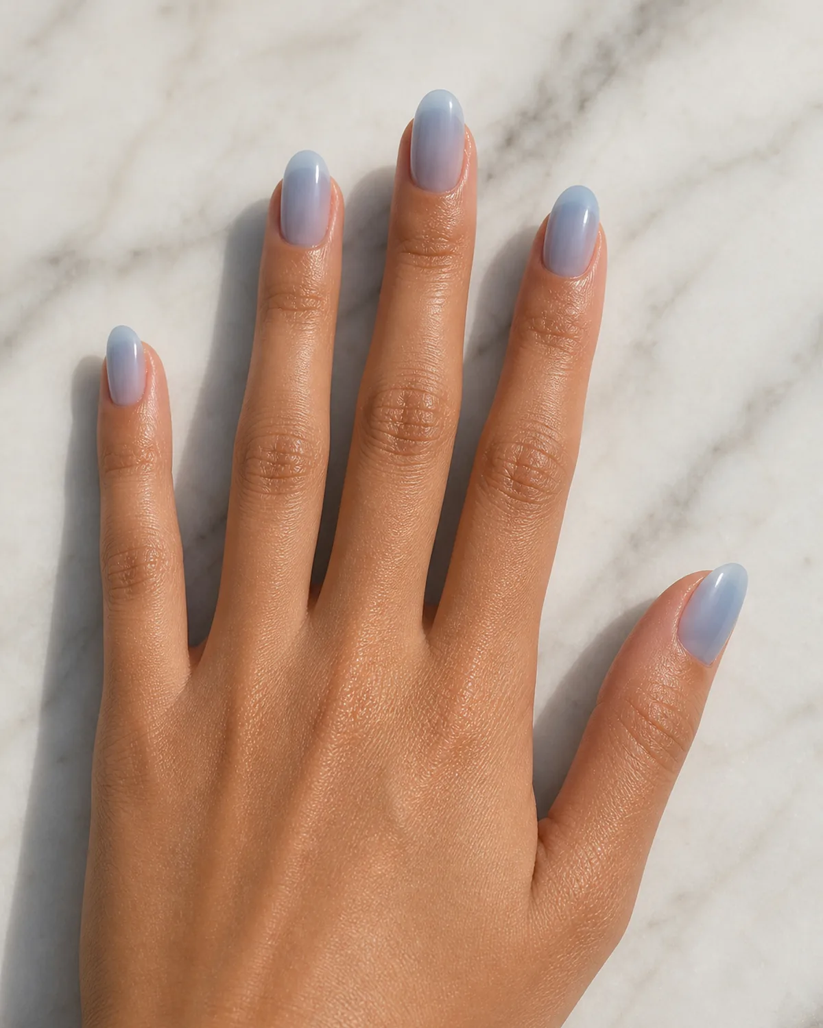 Close-up of medium oval nails in a cool sky-blue jelly polish covering the entire nail with both side walls curving inward to a soft even U-shaped free edge, on medium skin with fingers spread wide flat top-down on pale marble