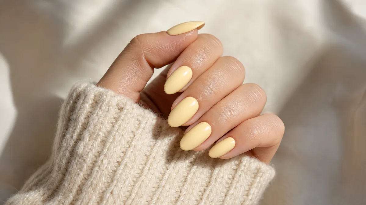 Side-angle close-up of almond nails in a soft, creamy butter yellow with the hand resting over a chunky cream knit sleeve