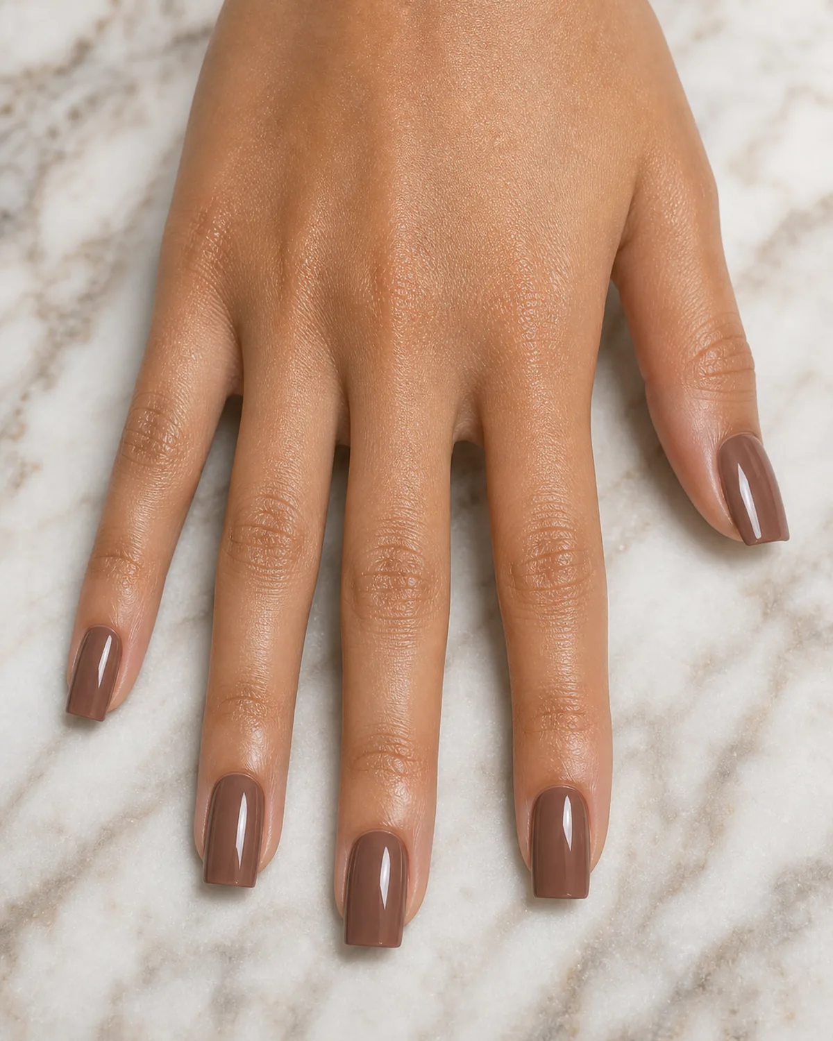 Close-up of medium square nails in a warm cocoa creme polish covering the entire nail with both side walls perfectly straight and parallel, free edge flat horizontal and tip corners sharp at 90 degrees, on medium skin with fingers spread wide flat top-down on pale marble