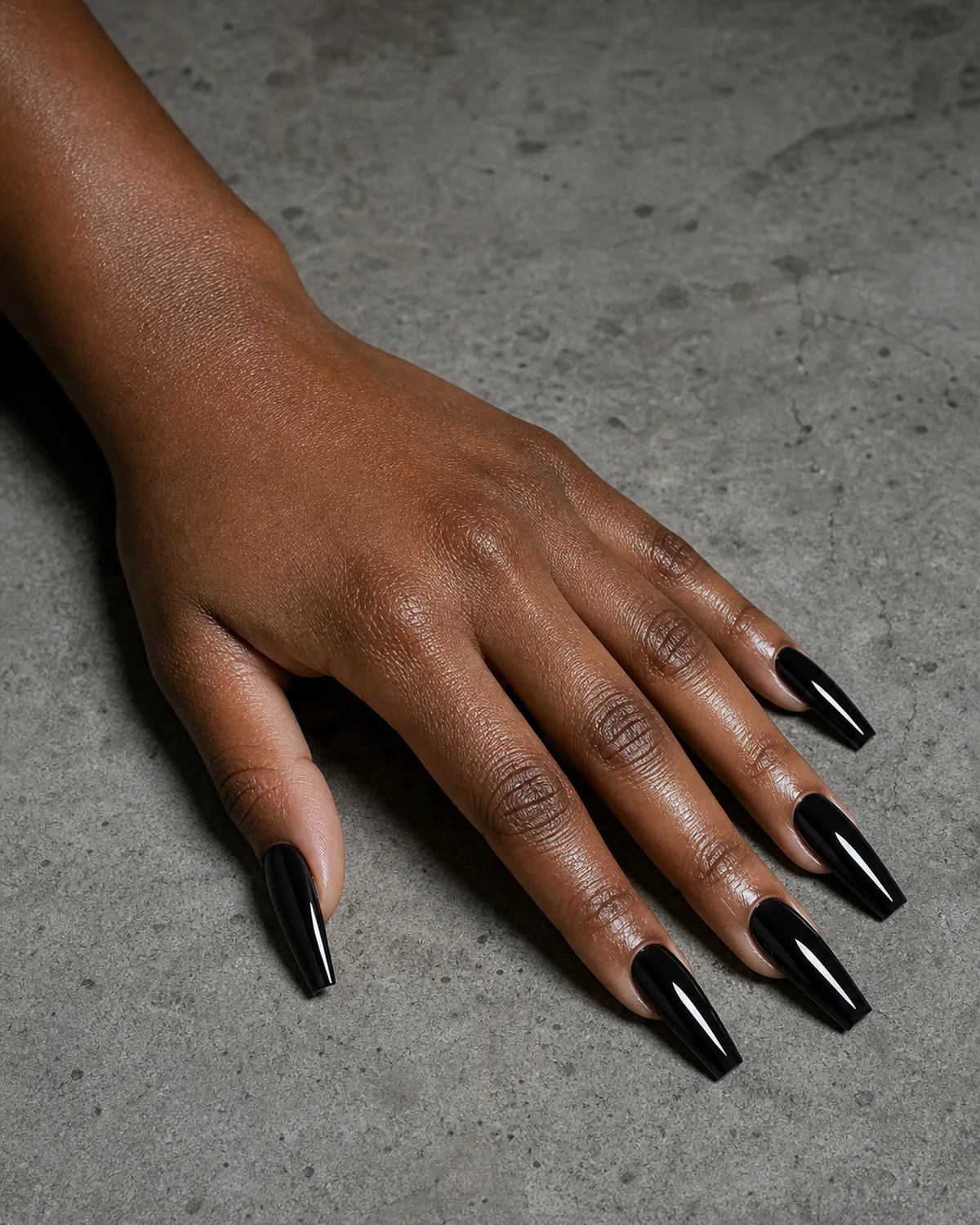 Long coffin acrylic nails in high-gloss black on grey concrete surface