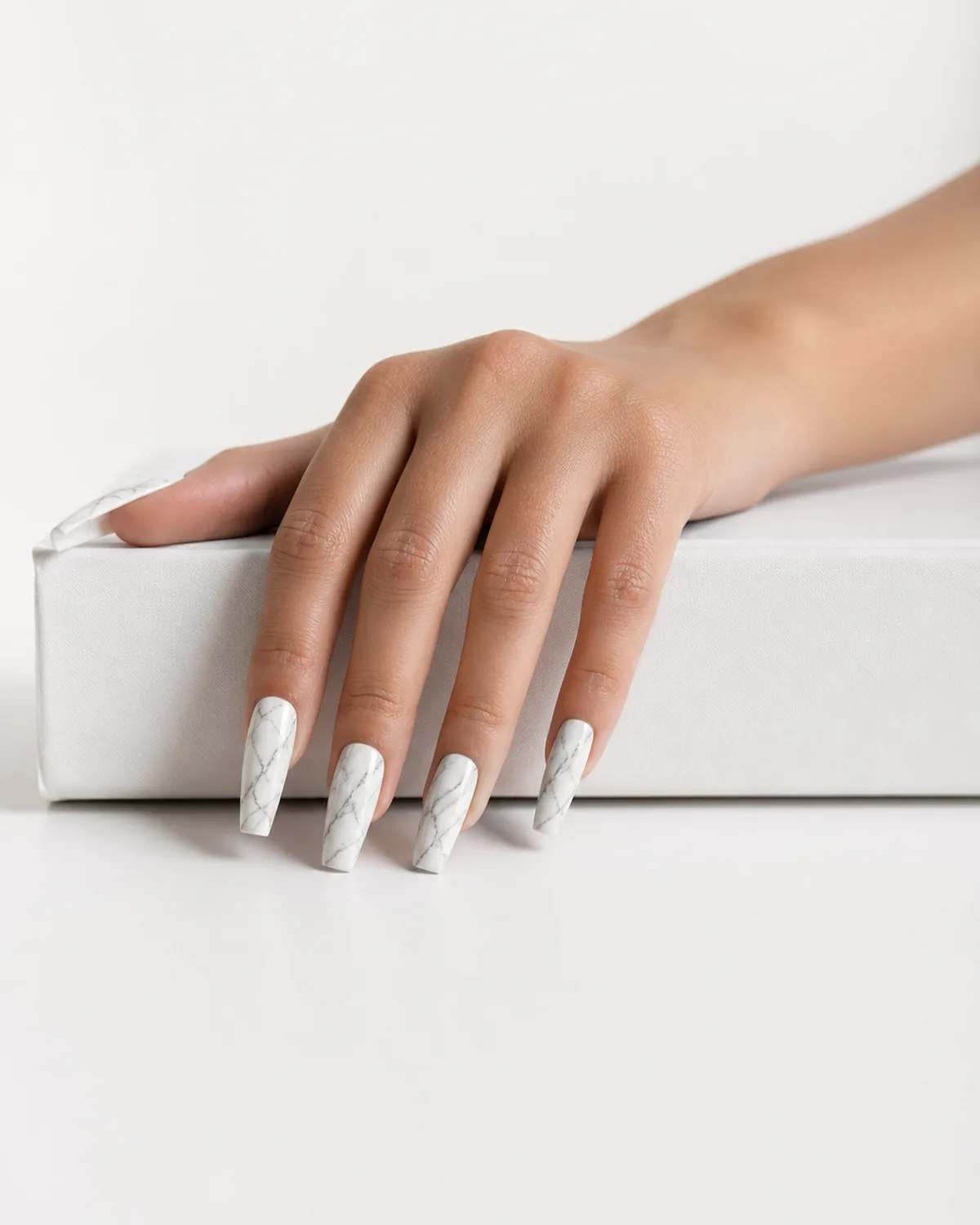 Long coffin acrylic nails with white-grey marble swirl effect draped over white book