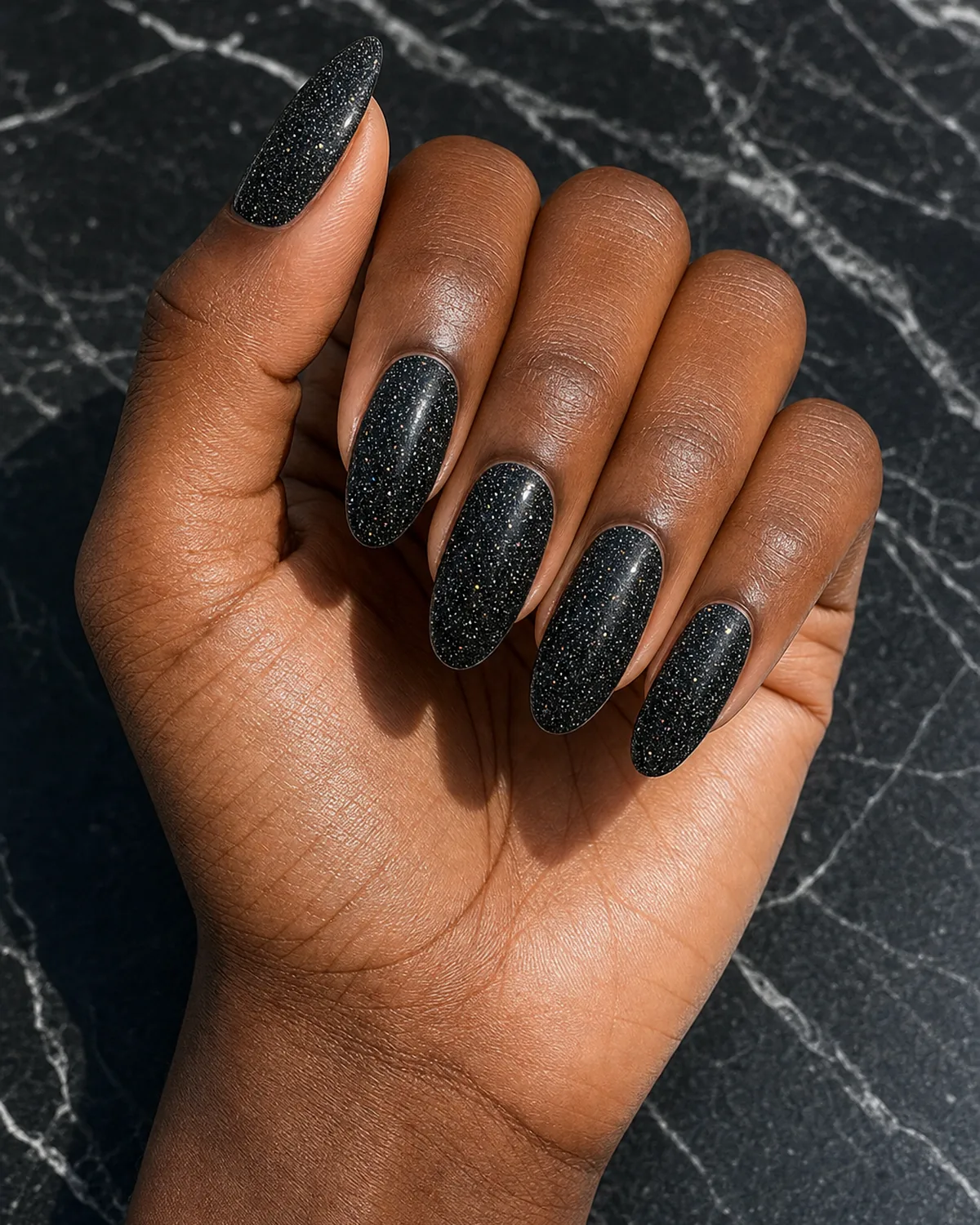 Black cream with scattered fine glitter on long oval nails