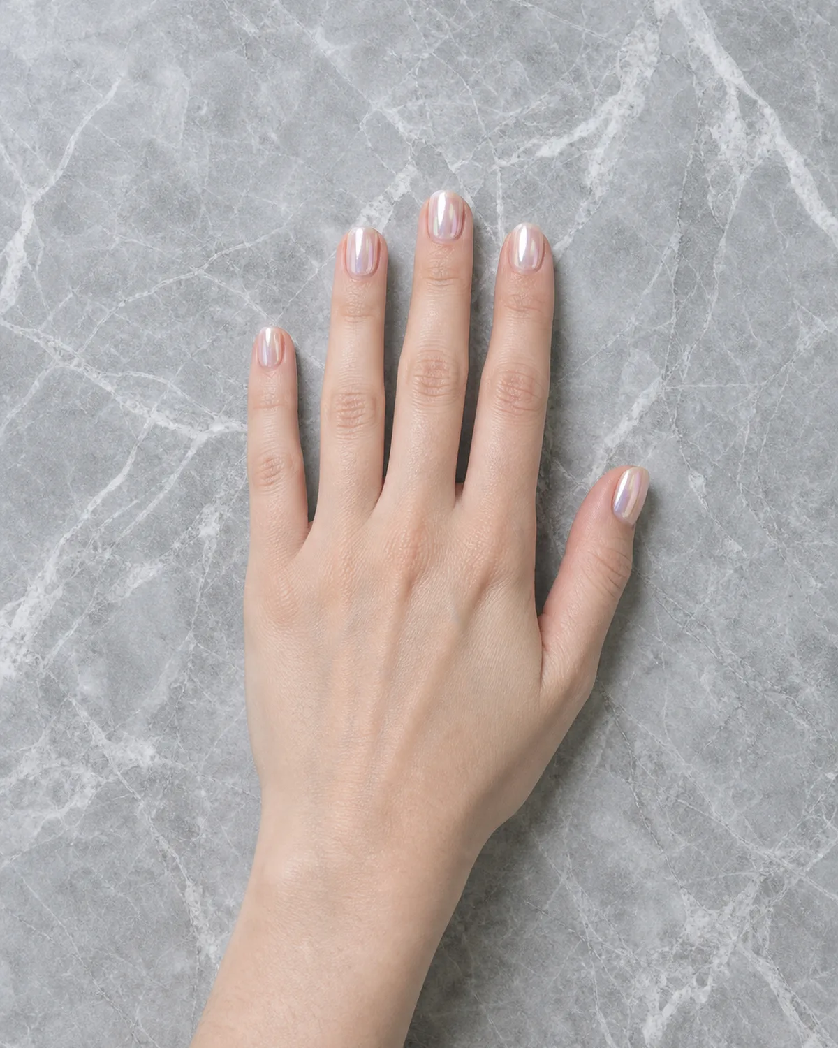 Single hand with glazed donut finish bridal nails on cool grey marble surface