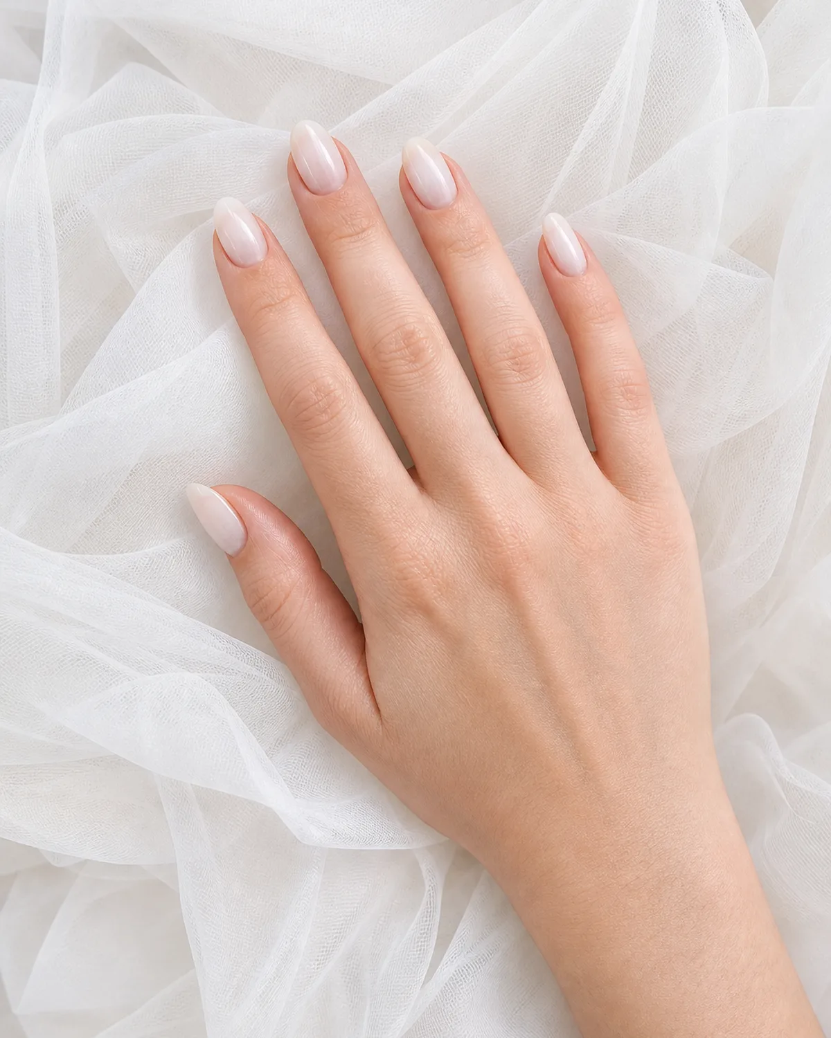 Single hand with milky white sheer gel bridal nails on white tulle fabric