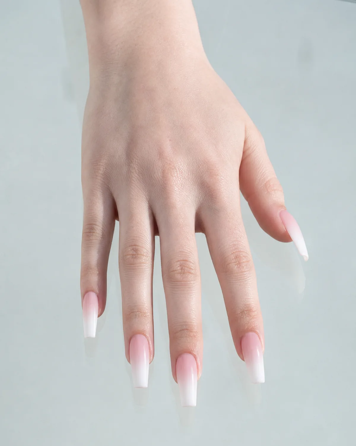 One hand palm-down on a glass surface with reflection visible, long coffin nails with French ombre gradient, light cool skin