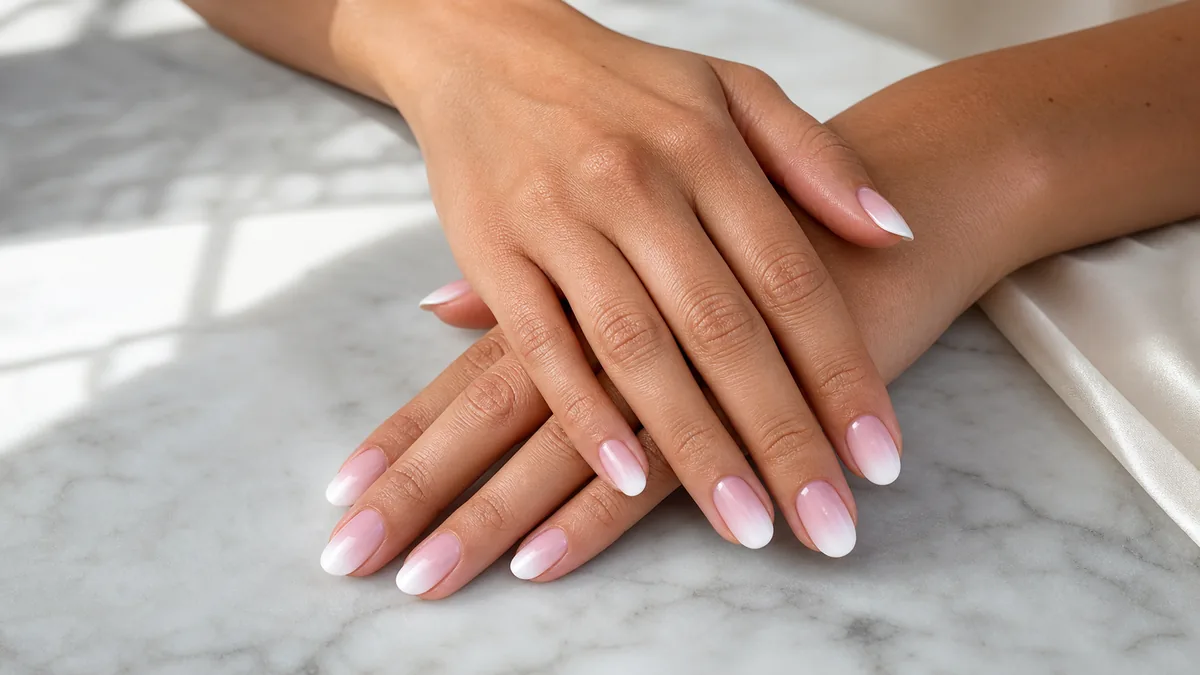 Two hands stacked with medium oval nails in a classic French ombre gradient, white tip fading to sheer pink, on white marble