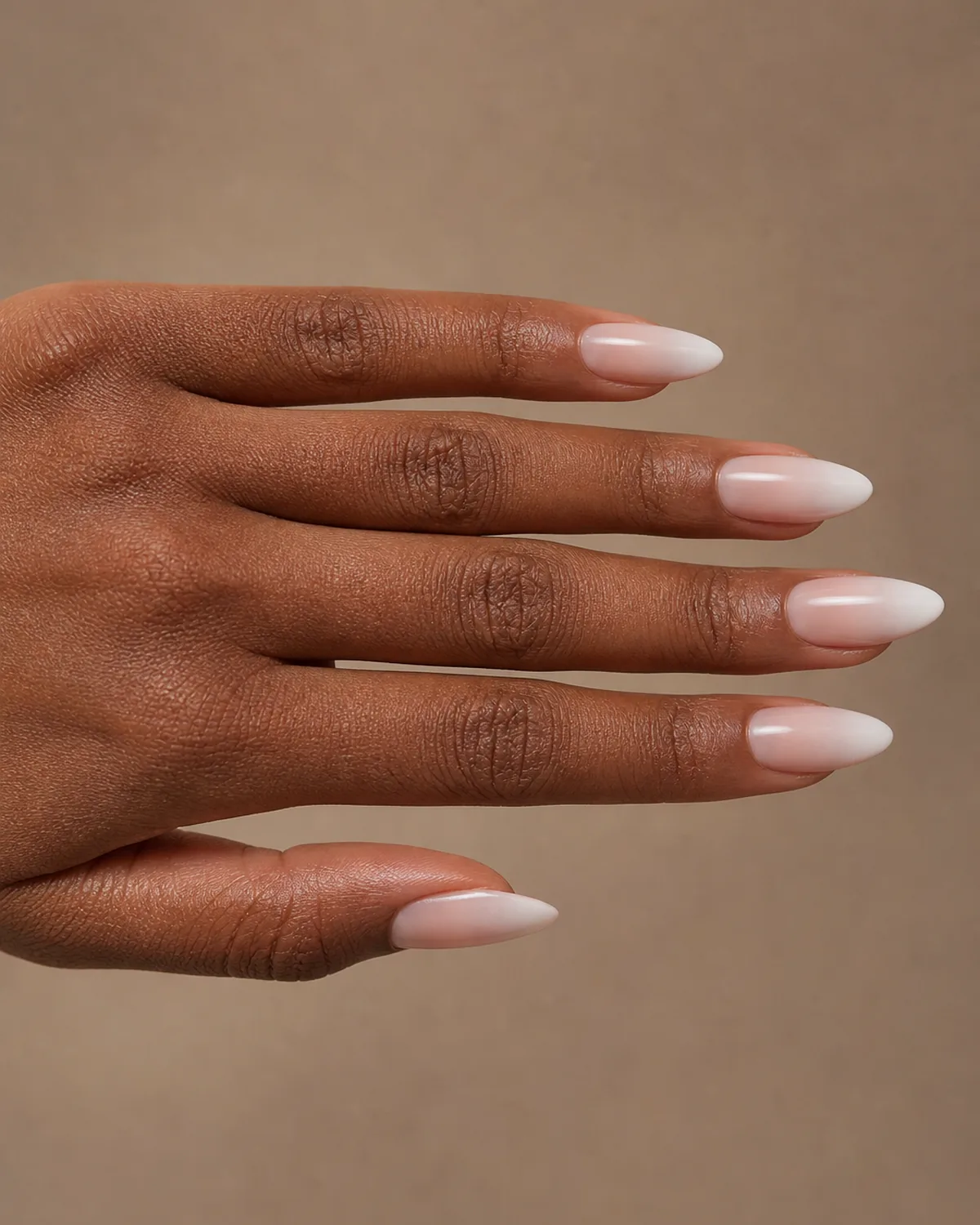 Side-profile of one hand with fingers extended, long almond nails with elongated French ombre gradient, deep warm skin