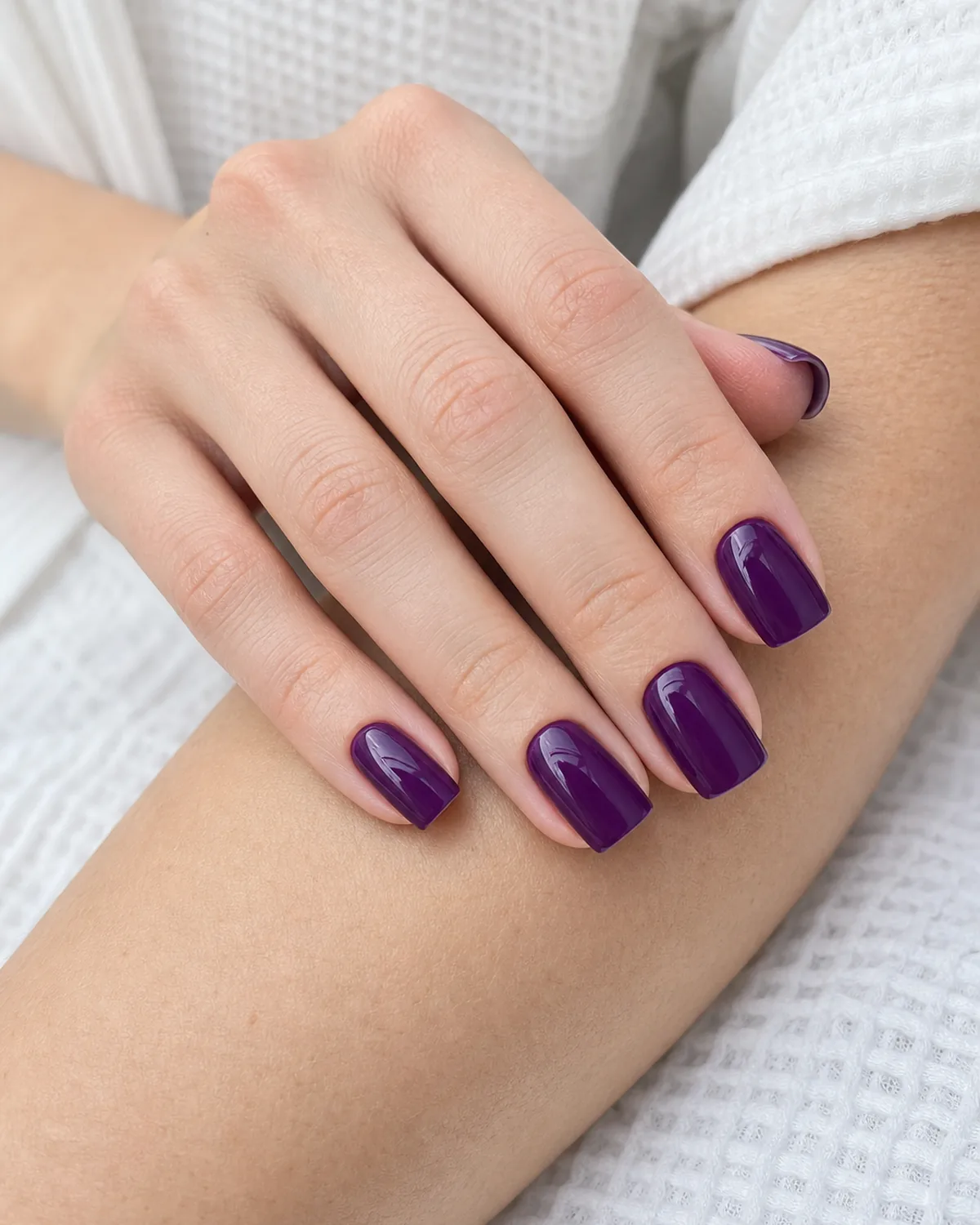 A saturated deep grape-purple on medium square nails, a fair-skinned hand resting on the opposite forearm