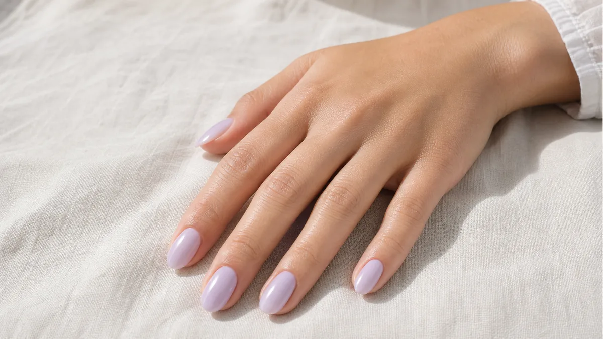 A close-up of a hand wearing the palest lilac wash on medium almond nails, resting flat on pale linen in soft daylight