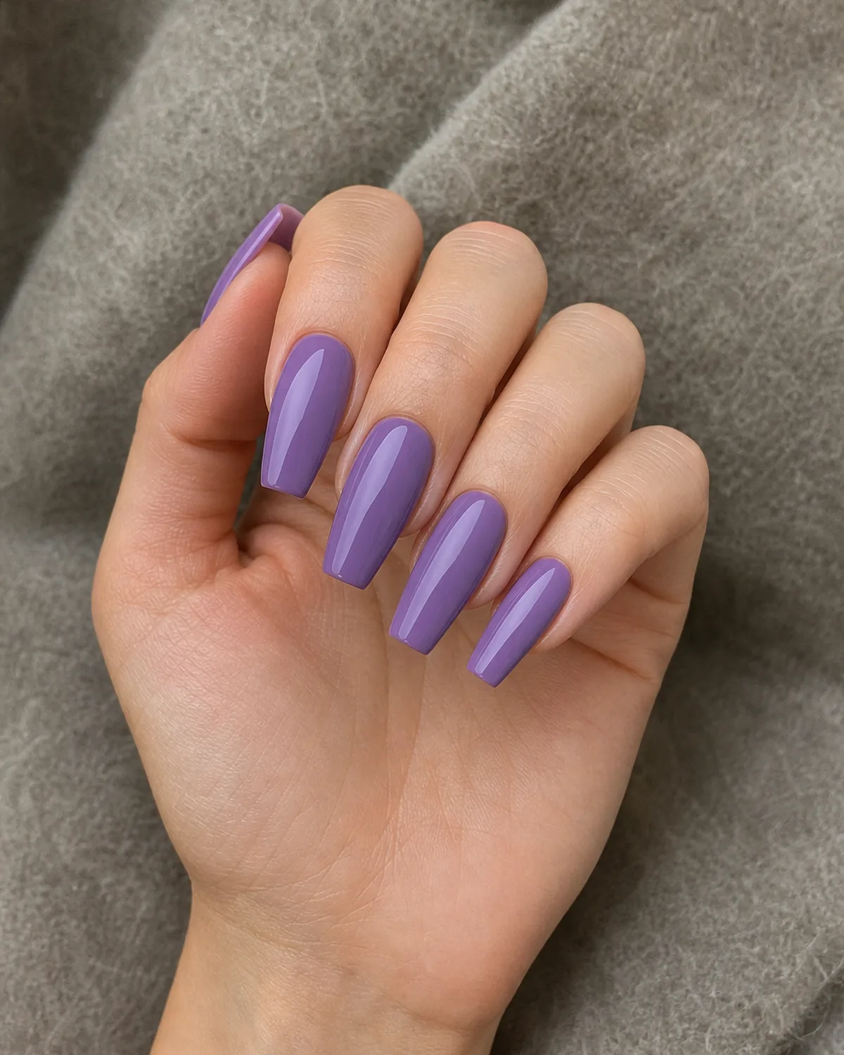 A mid-tone transitional purple on coffin nails, a light-medium-skinned hand half-raised with fingers loosely curled