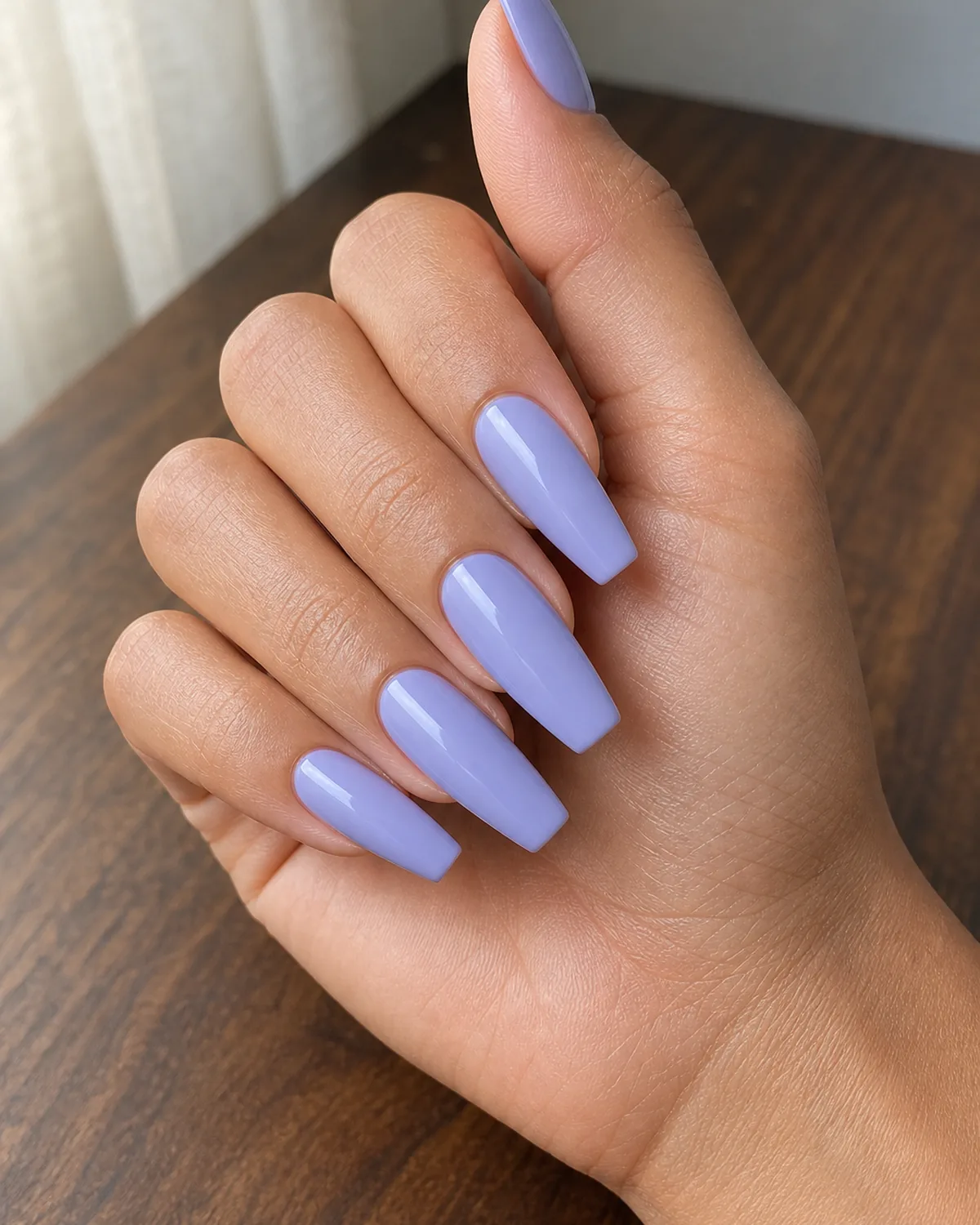 A periwinkle-leaning lavender on long coffin nails, a tan-skinned hand resting on warm walnut wood