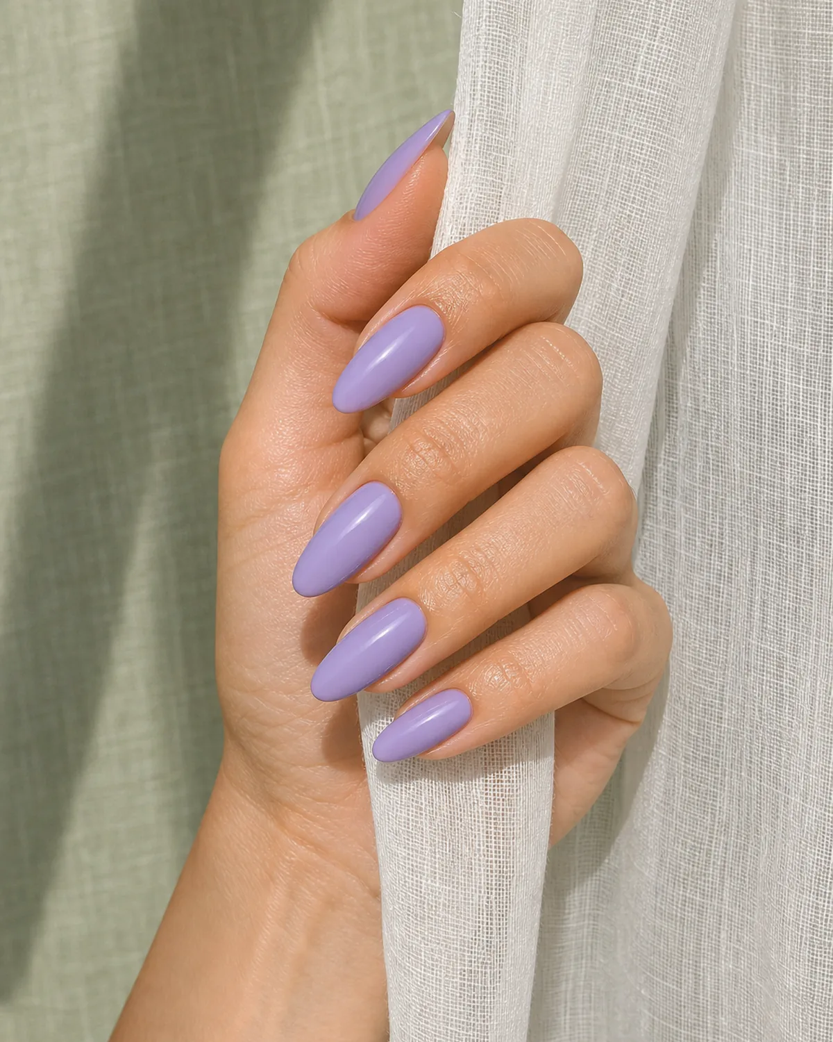A true-to-swatch daylight lavender on long oval nails, a light-medium-skinned hand holding a sheer curtain edge
