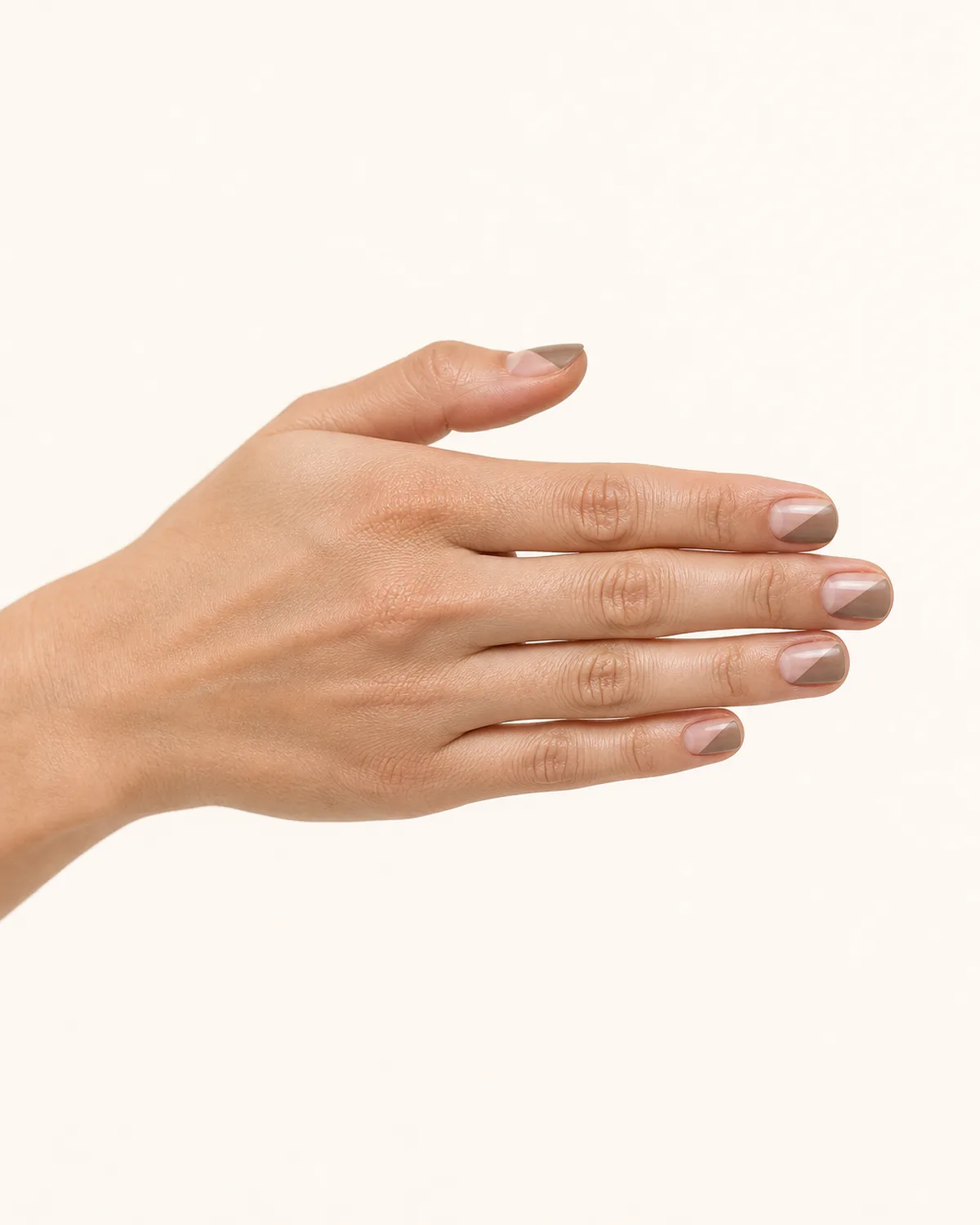 Side profile of a hand with fingers extended showing short square nails with a diagonal half-painted design in warm taupe