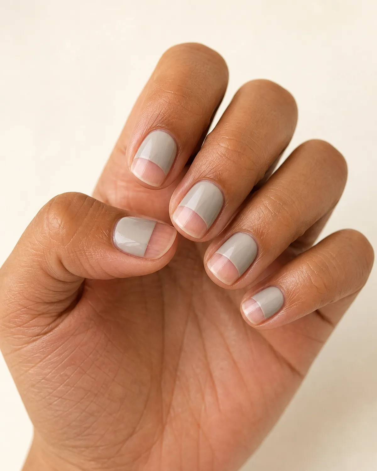Close-up macro of fingers in a soft curl showing short square nails with half-moon negative space design, lower half bare and upper half in soft greige