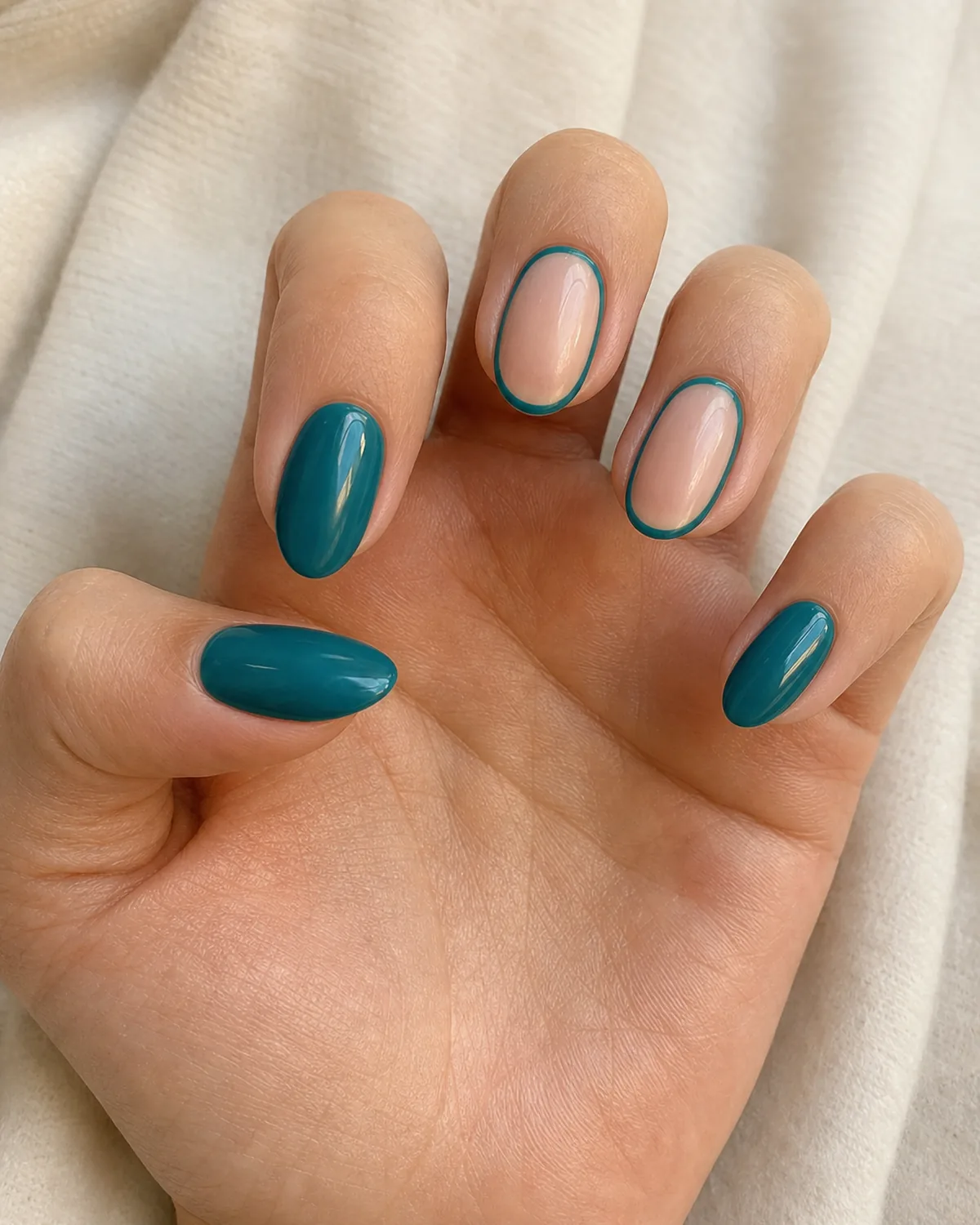 Close-up of medium oval nails mixing negative-space outline designs with fully covered solid nails in the same color, on light-medium skin with palm open