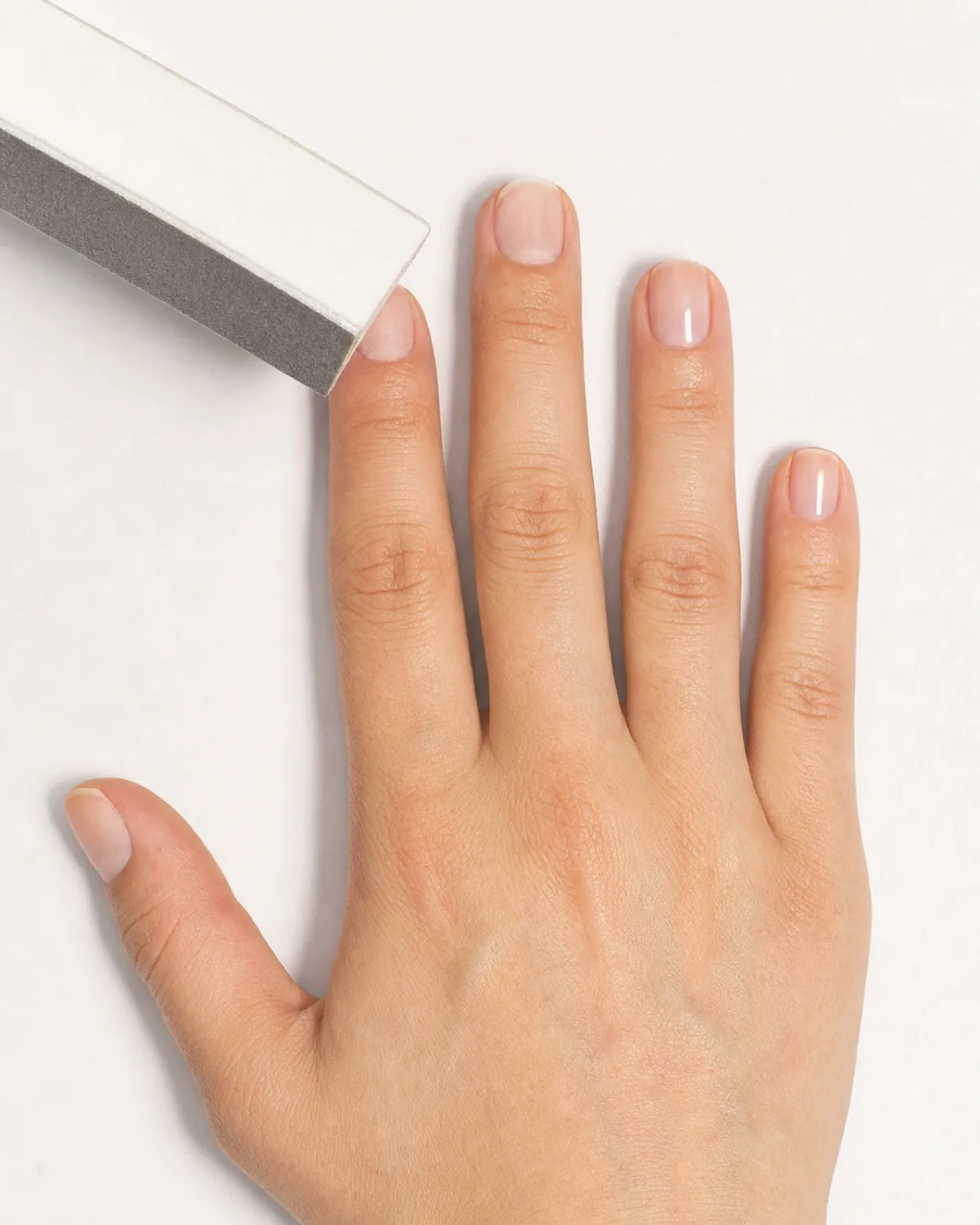 Overhead view of a hand being buffed with a four-way buffer block, some nails showing mirror shine and others still matte
