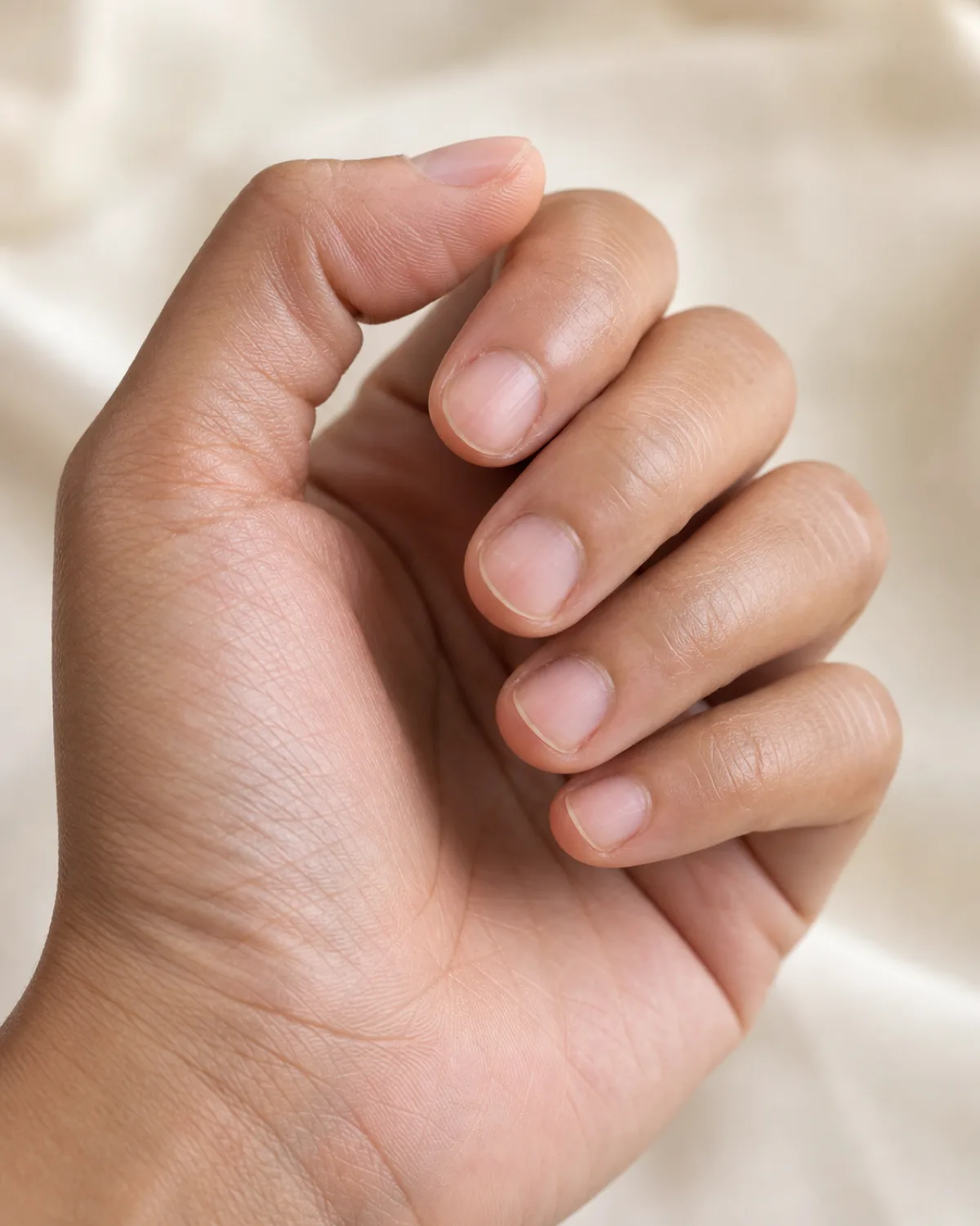 Macro close-up of a hand with short natural nails in a soft claw pose, showing strong healthy nail tips