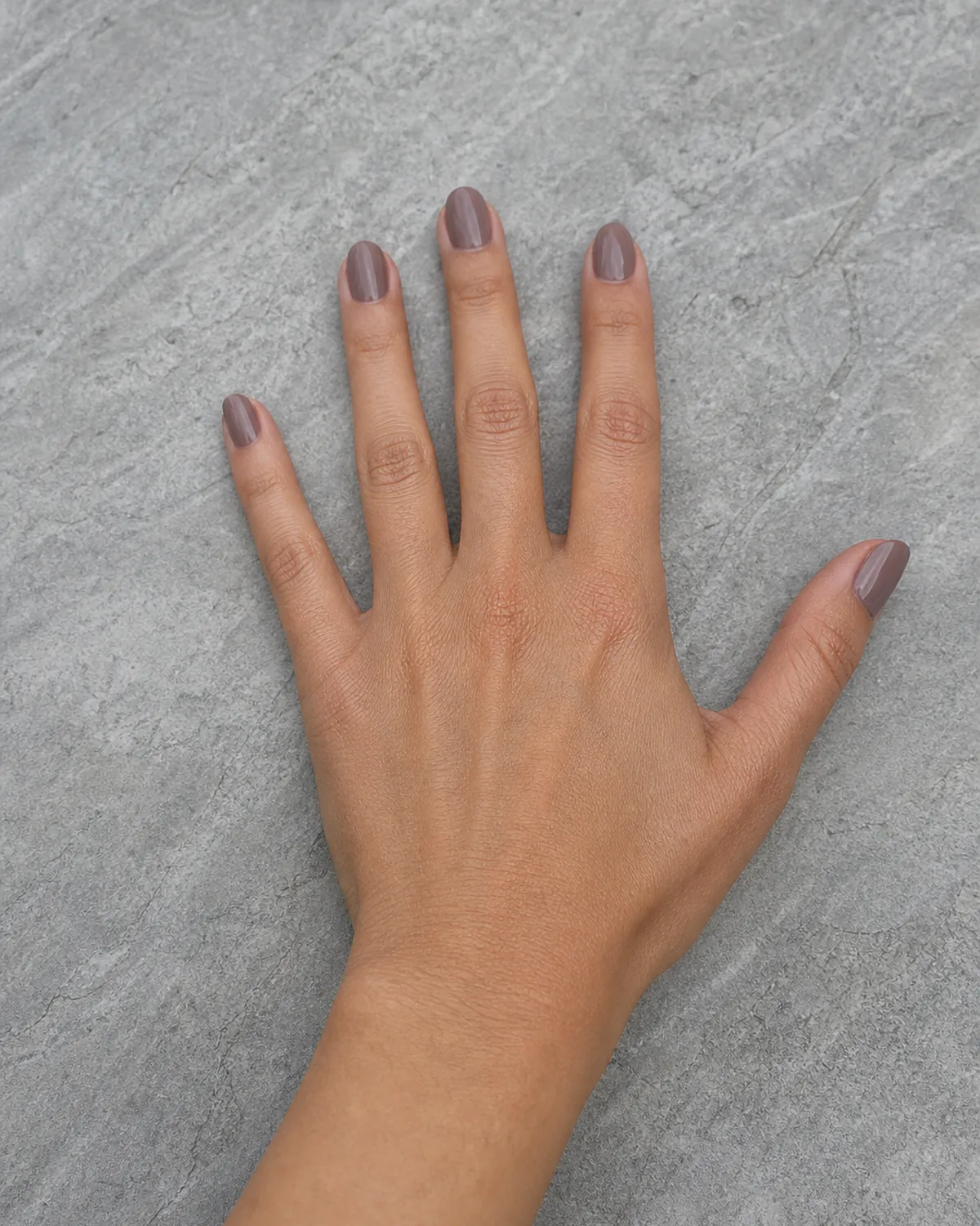 Single hand with mushroom-toned nail polish resting on raw stone surface