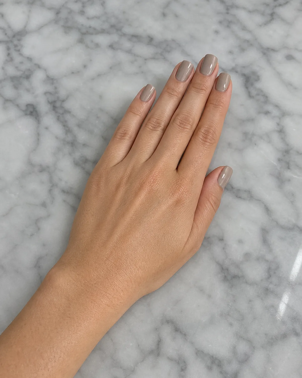 Single hand with true neutral gel nails resting on grey-veined marble countertop