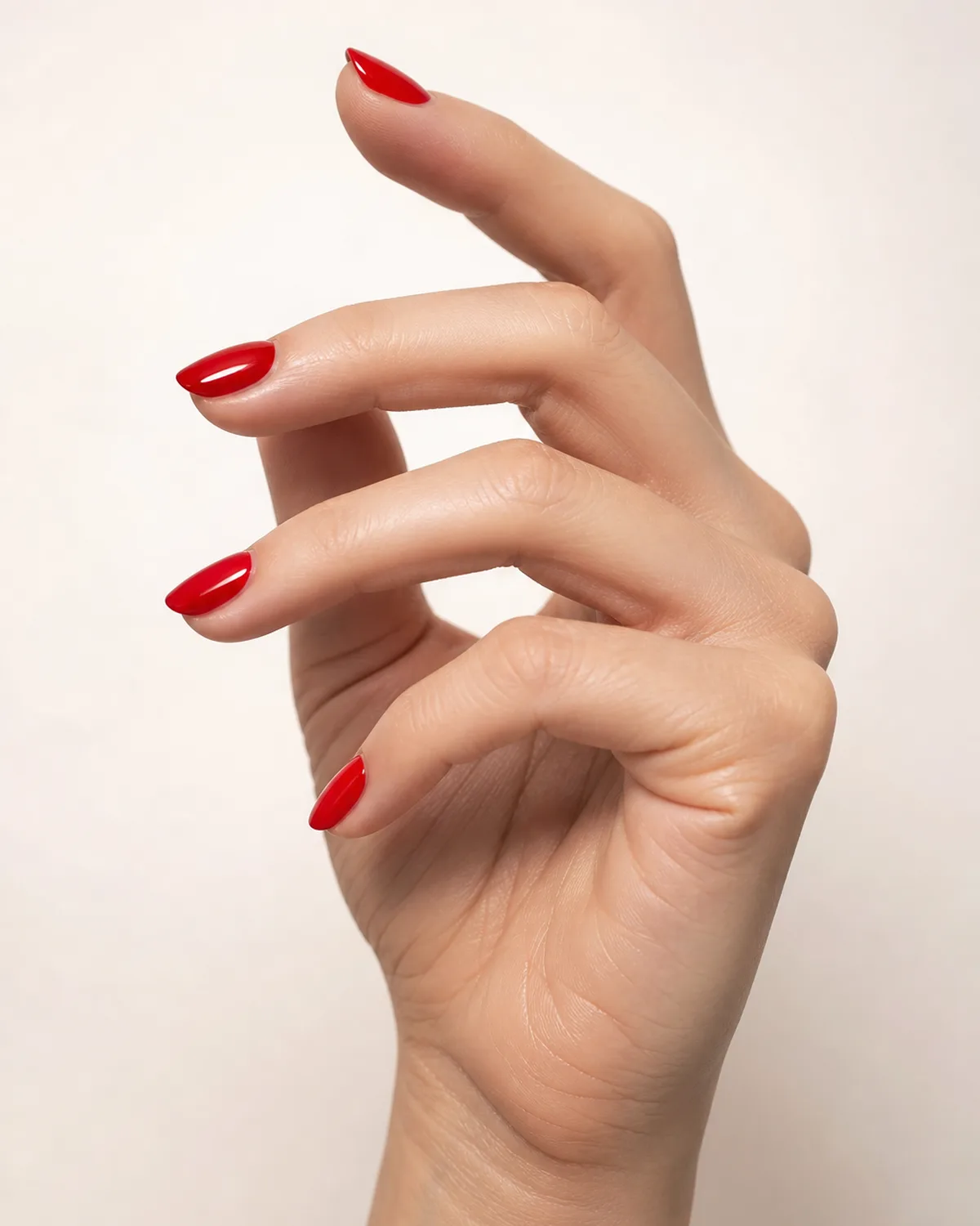 Three-quarter angle of a hand with short pointed acrylic nails in bold cherry red, fingers elegantly extended