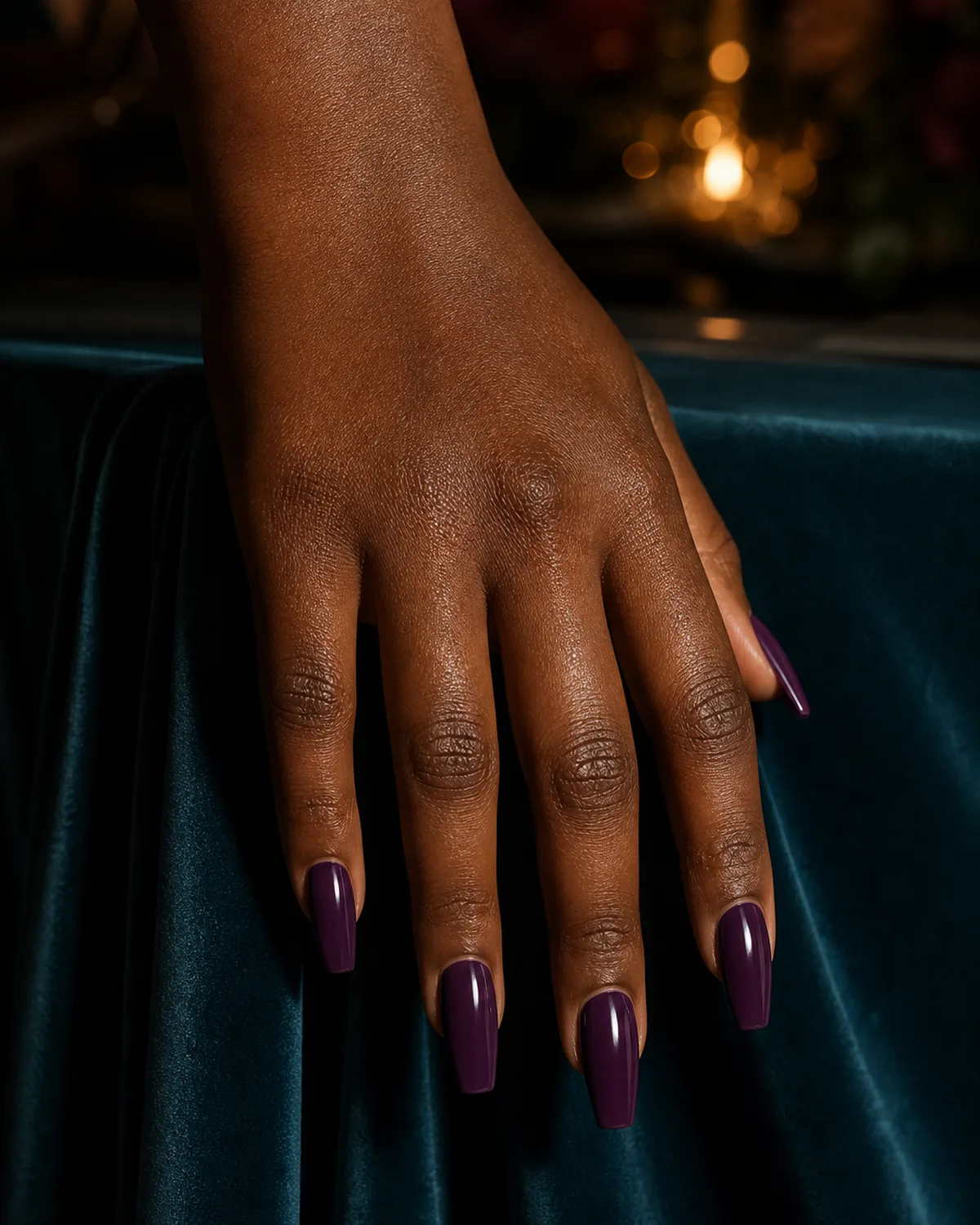 Rich deep plum on medium coffin nails against dark teal fabric, dramatic side lighting