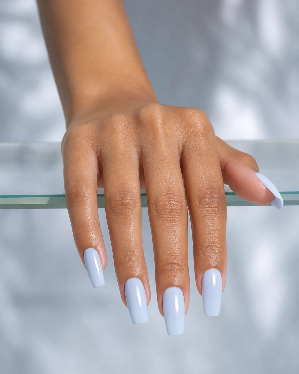 Single hand with ice blue nails on medium coffin shape draping fingers over the edge of a clear glass shelf