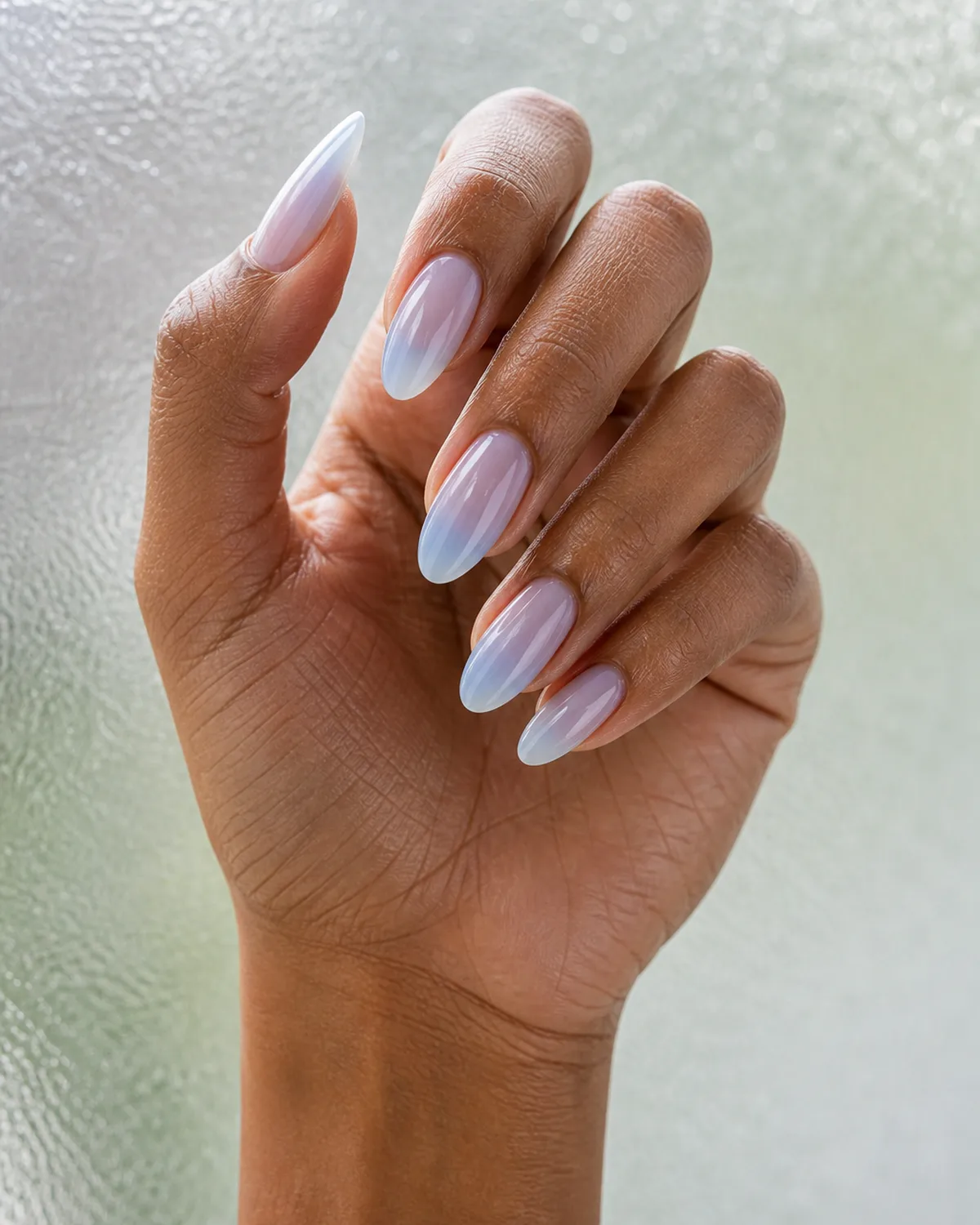 Single hand with ice blue jelly nails on long almond shape showing translucent polish with nail bed visible beneath resting on frosted glass