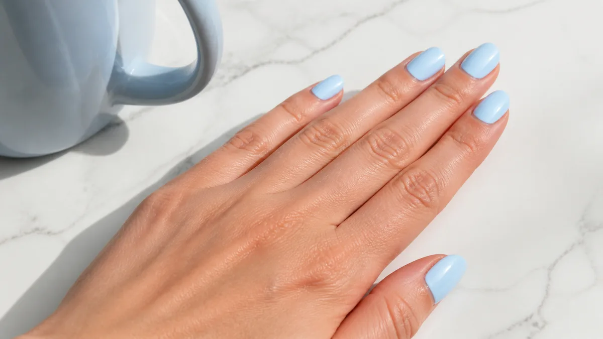 Single hand with classic baby blue pastel nails on short almond shape resting on white marble beside a pale blue ceramic mug