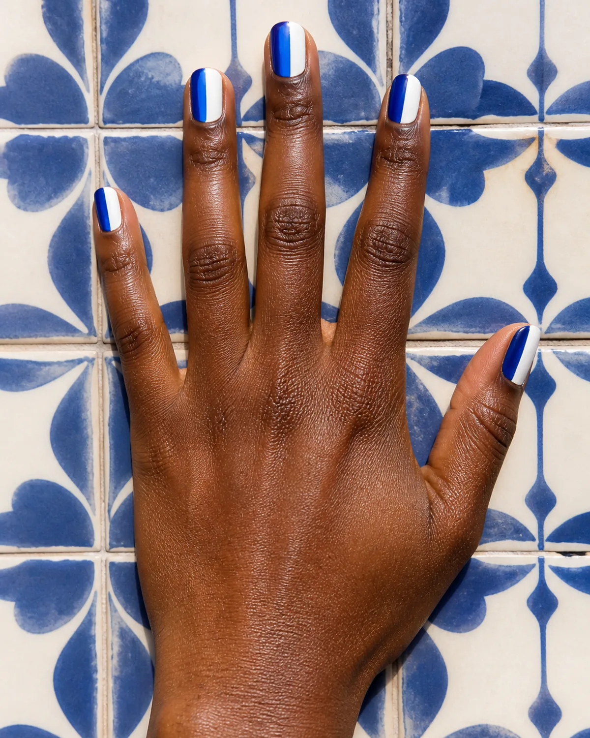 Single hand with cobalt blue and white color-block nails on squoval shape splayed flat palm down on blue-and-white ceramic tile