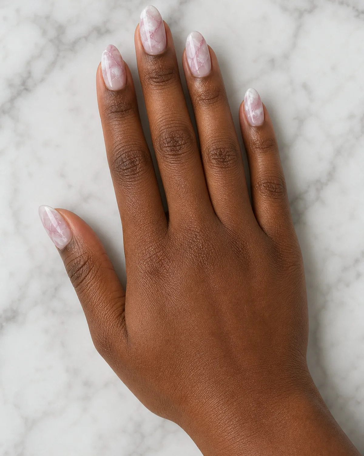 Single hand with translucent white base and soft pink and mauve swirled rose quartz veining on medium almond nails on white marble slab
