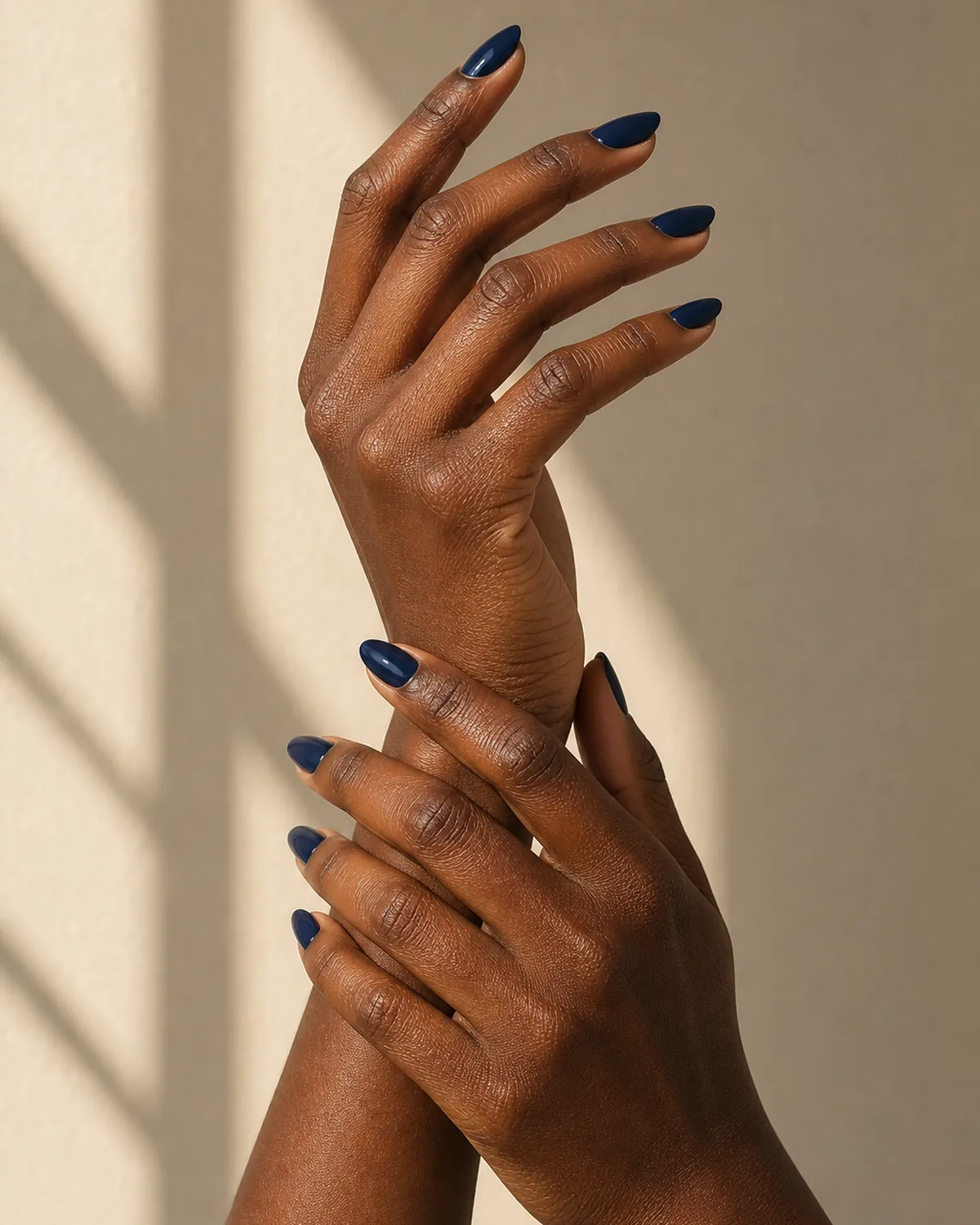 Two hands vertical with one loosely holding opposite wrist showing deep navy blue polish on almond nails