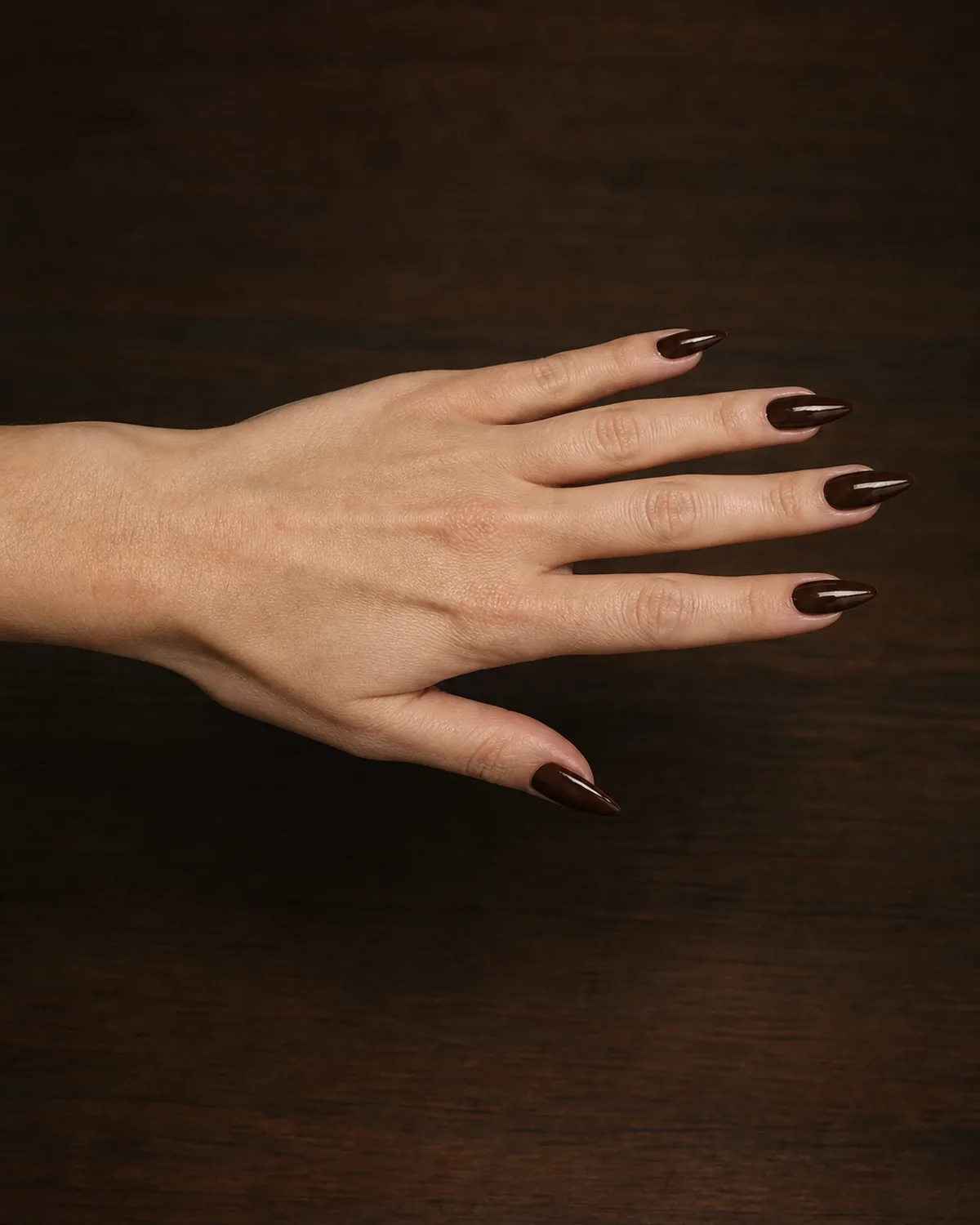 Side profile of one hand with fingers extended showing deep espresso brown glazed polish on medium stiletto nails