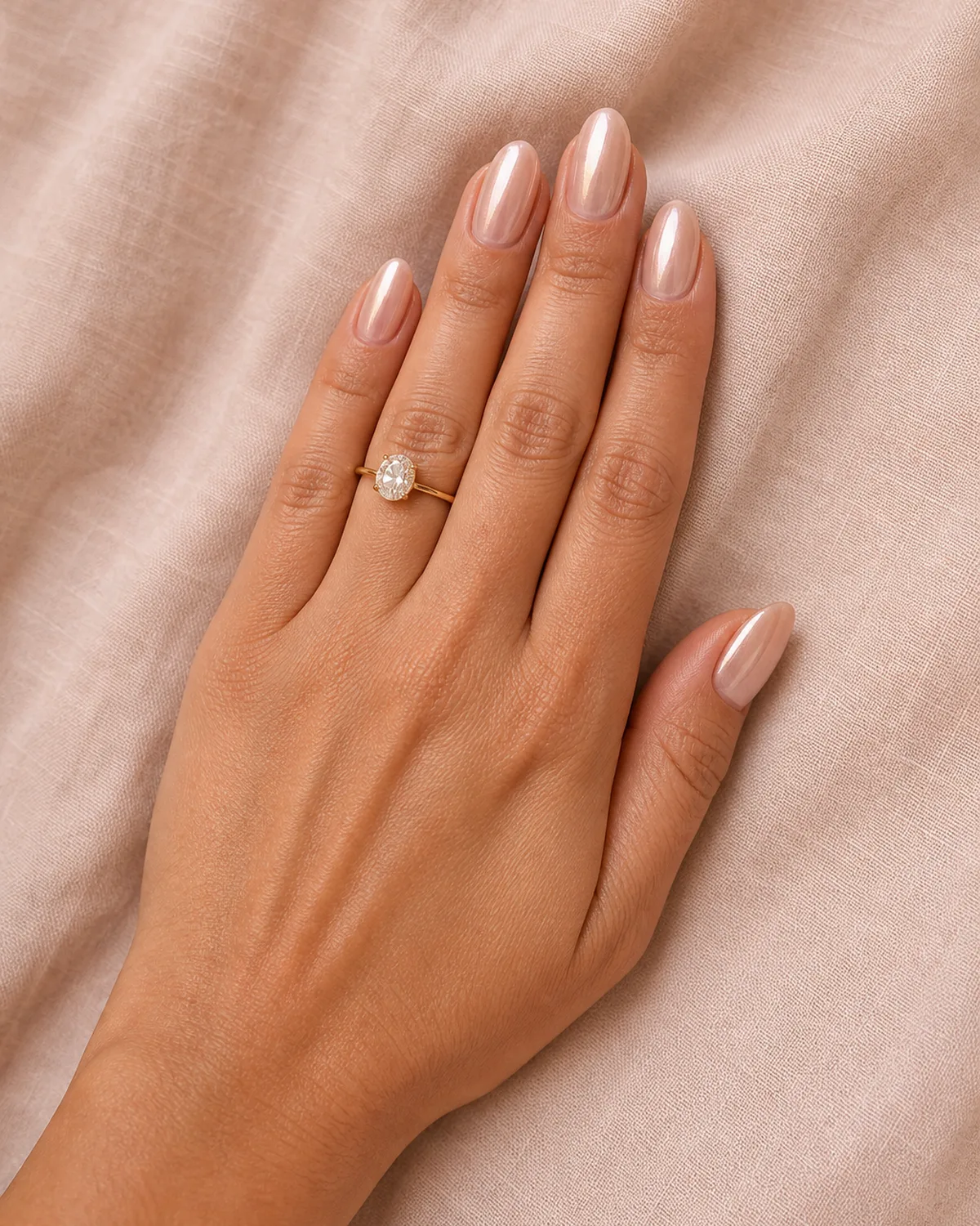 Single left hand with glazed donut chrome powder finish on medium almond nails on blush linen fabric with engagement ring visible on ring finger