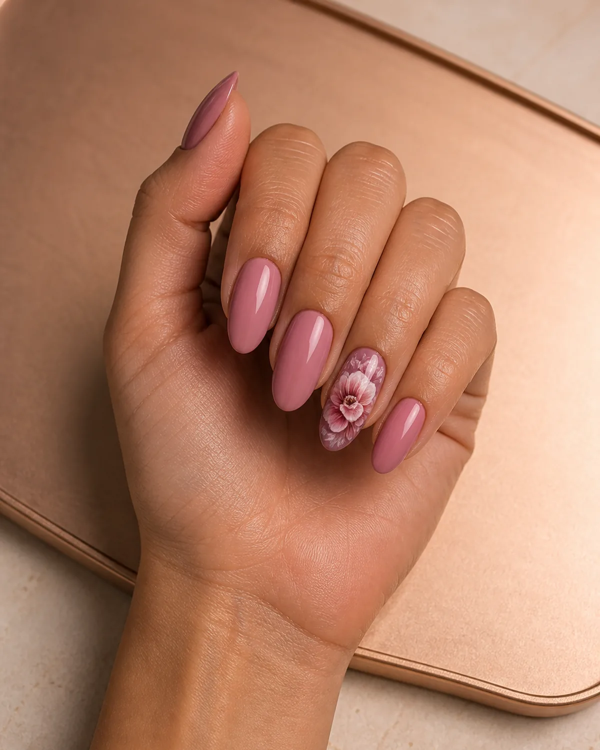 Single hand with oversized lush peony bloom in dusty pink and mauve on one statement nail with remaining nails matching dusty pink long oval shape on pale rose-gold tray