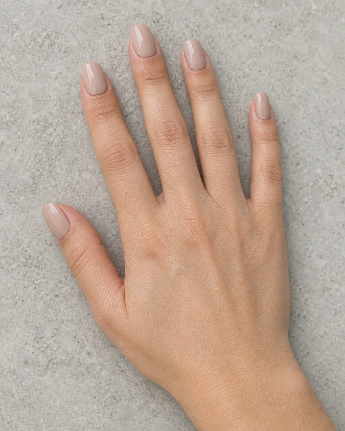 Close-medium detail of a single hand with four glossy nude press-on nails applied, a tiny air bubble visible under the pinky nail edge
