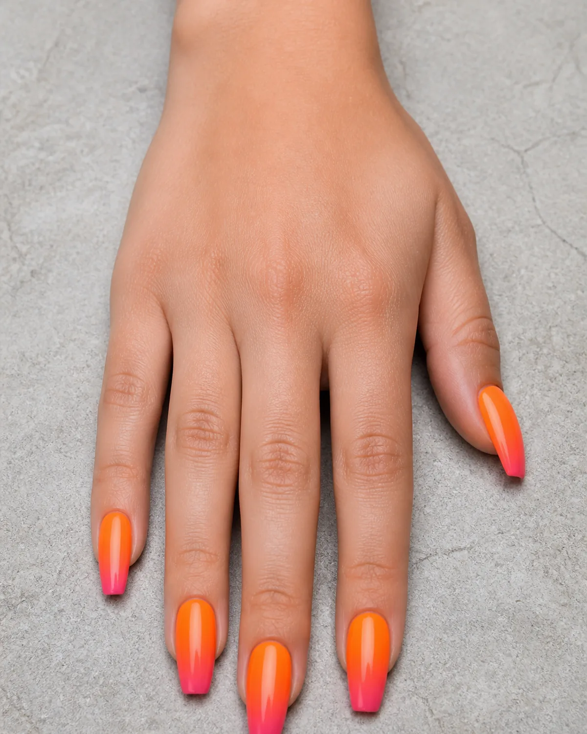 Single hand with gradient from warm orange at cuticle fading to soft pink at tip on medium coffin nails resting on pale gray stone surface