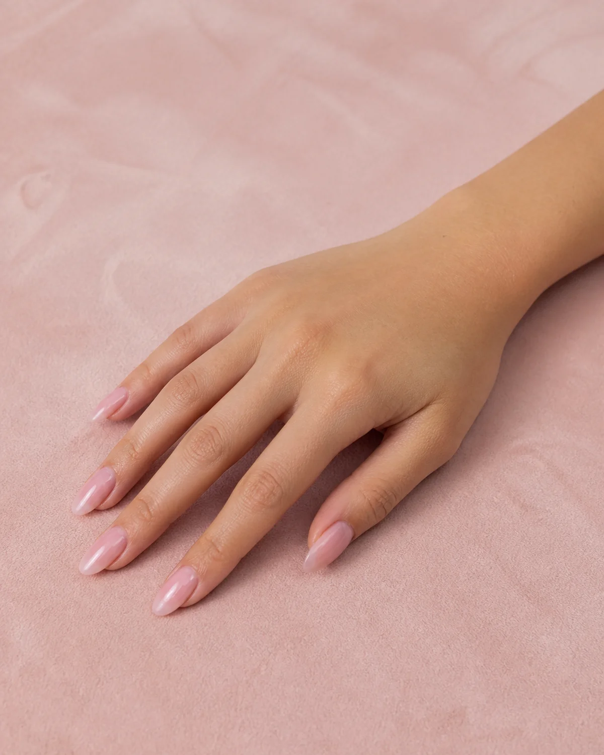 Single right hand with sheer baby pink jelly nails on long almond shape palm down on blush velvet surface