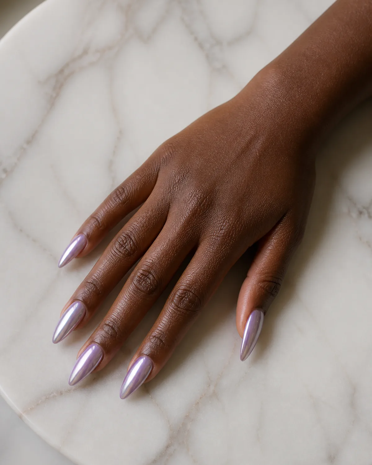 Single right hand with pearlescent lavender chrome stiletto nails palm down on white marble tray