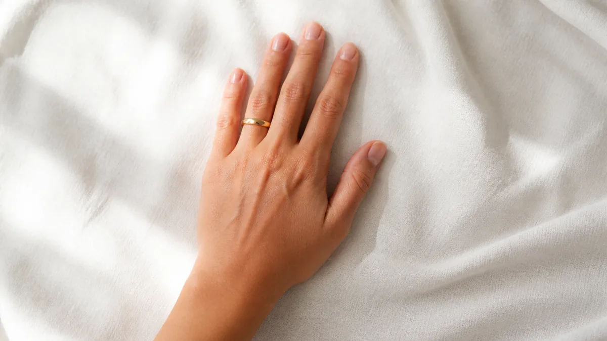 Single hand with sheer milky polish on short natural nails resting palm-down on ivory linen with gold wedding band