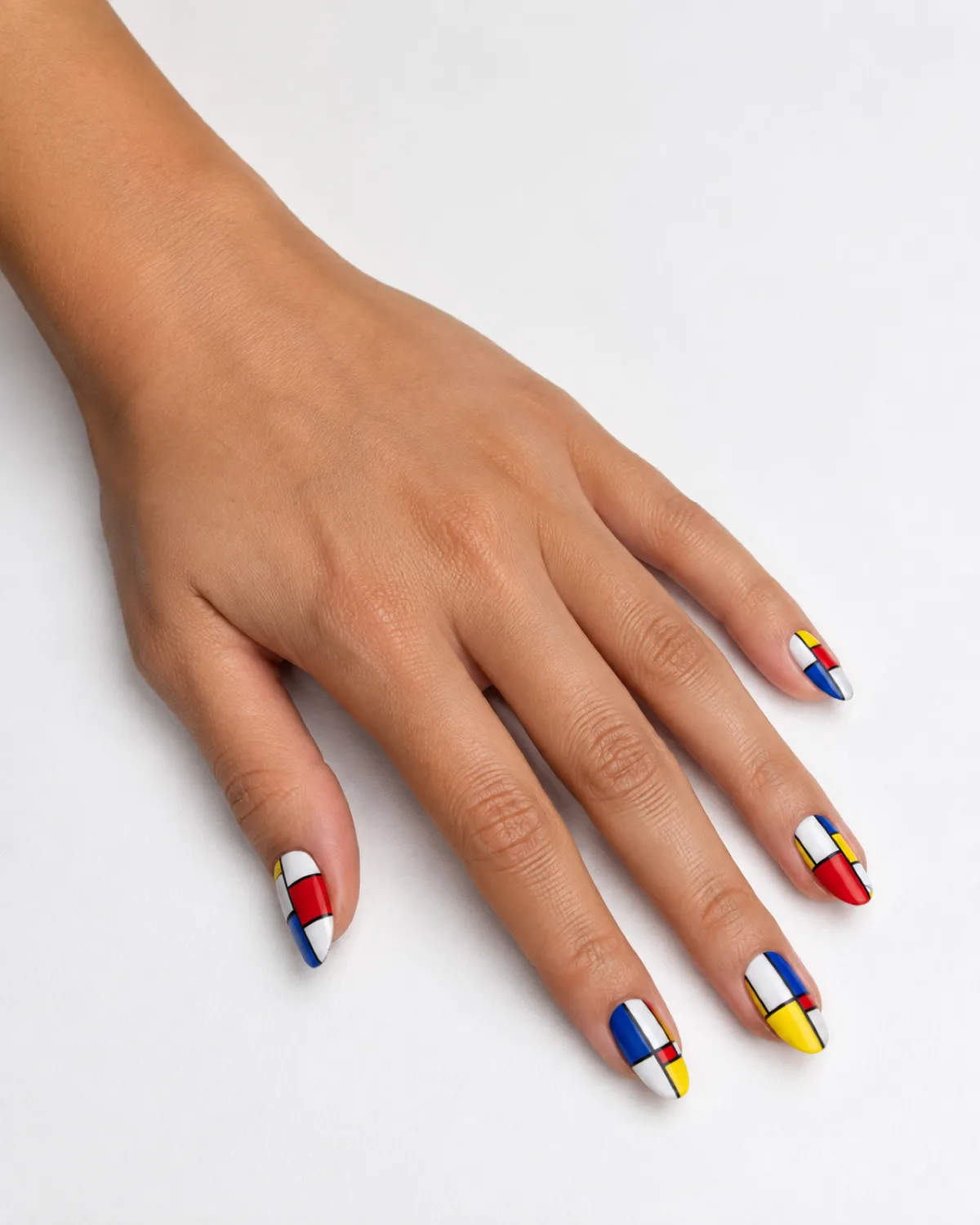 Single left hand with medium almond nails in Mondrian-style color-block panels of red blue and yellow on white surface