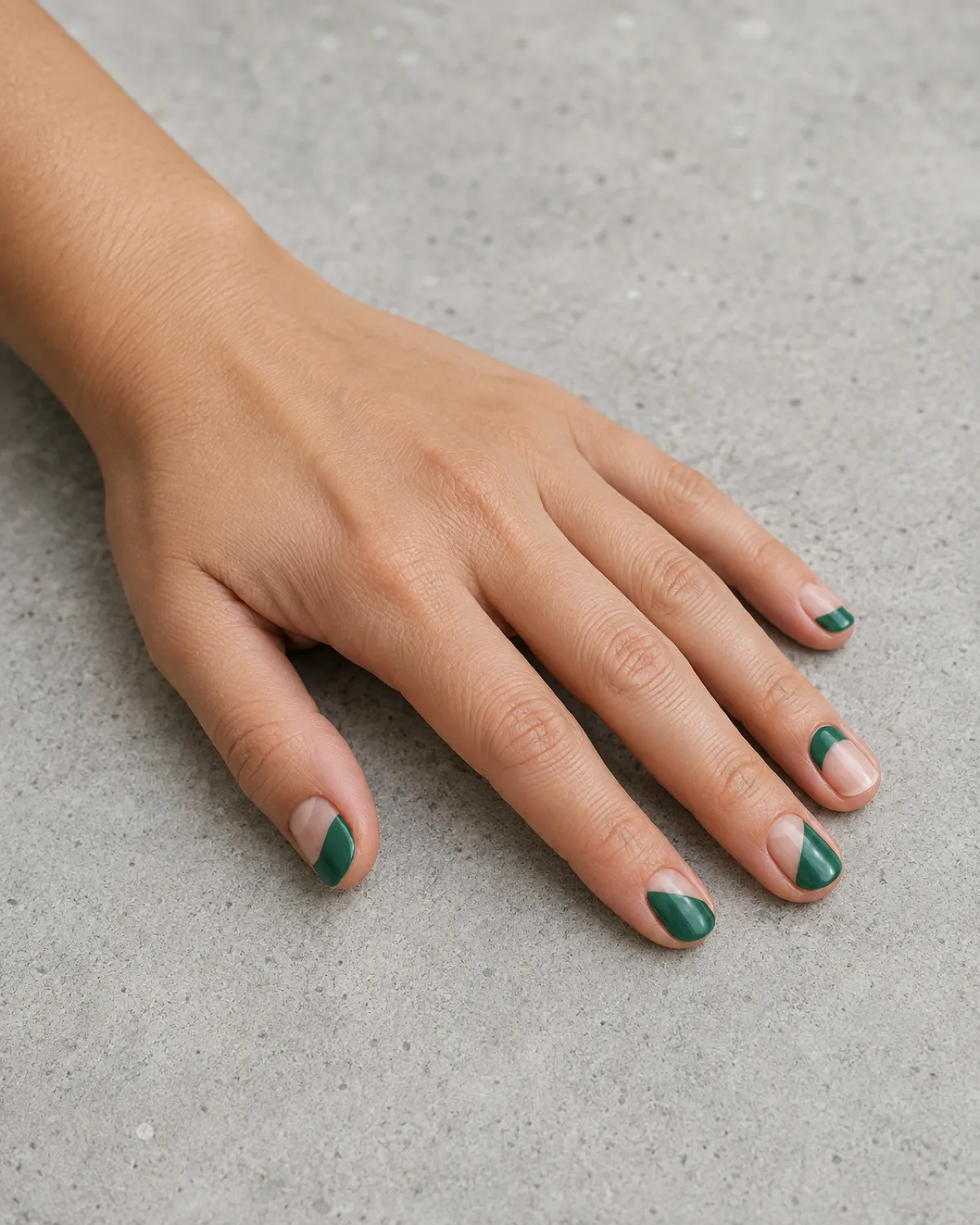 Single left hand with short oval nails in emerald green negative-space geometric cutout designs on grey concrete