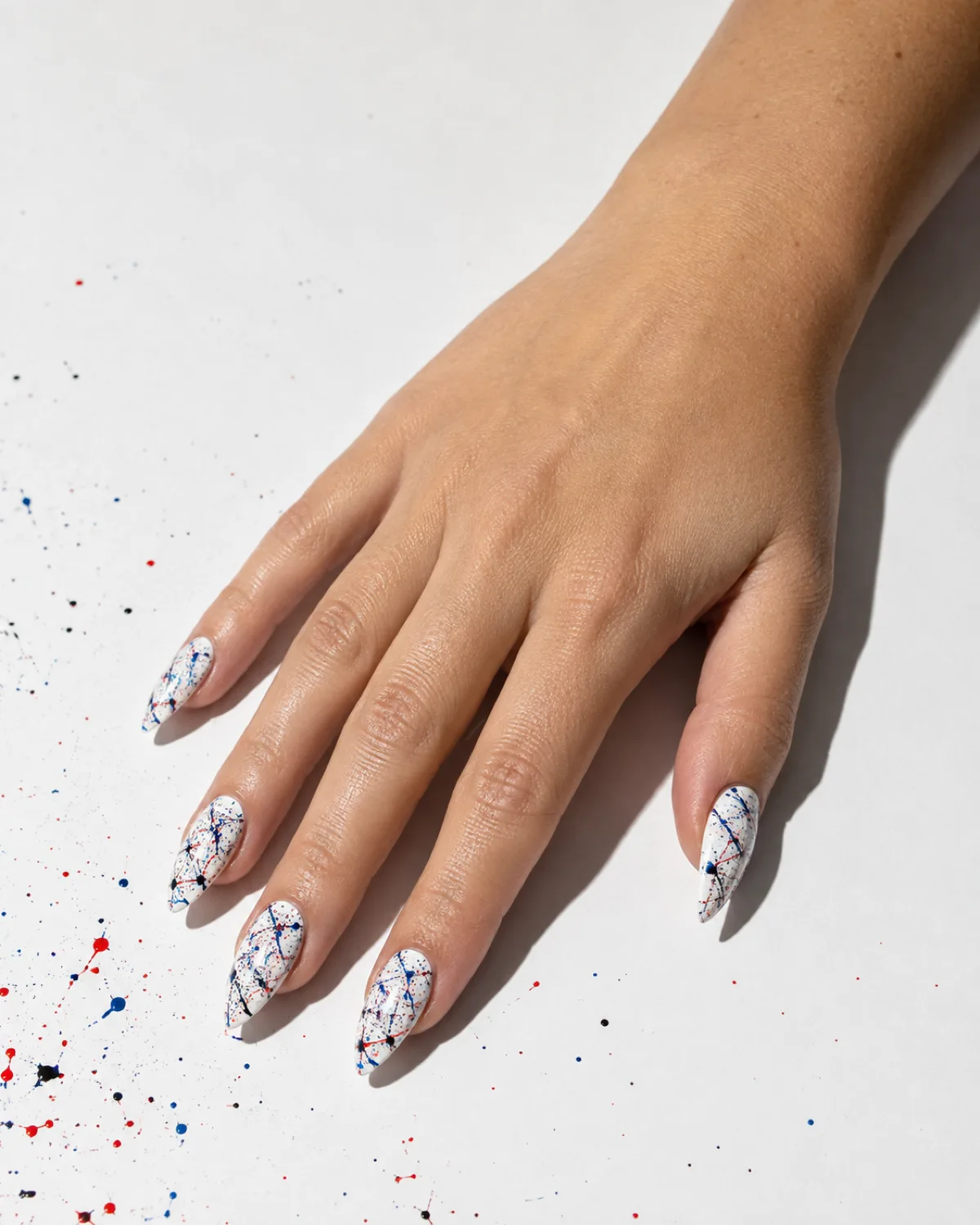 Single right hand with medium stiletto nails in chaotic paint splatter on white base with black red and blue drips on white paper