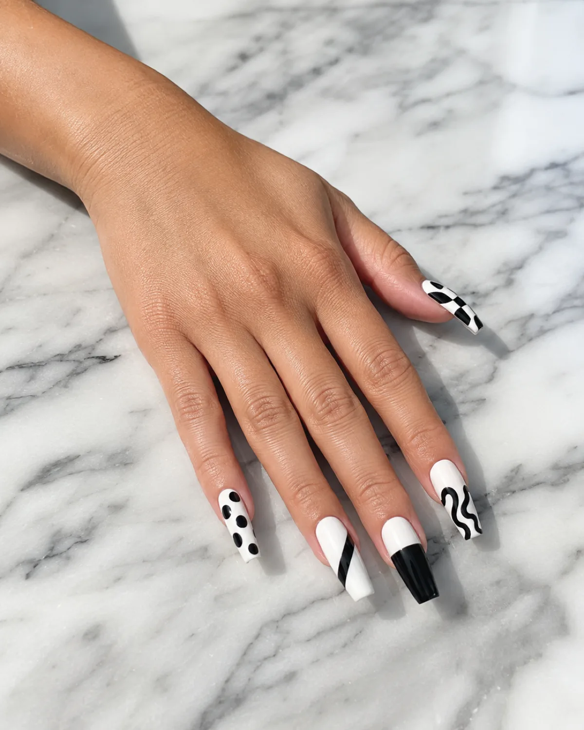 Single left hand with long coffin nails in graphic black-and-white abstract shapes on white marble