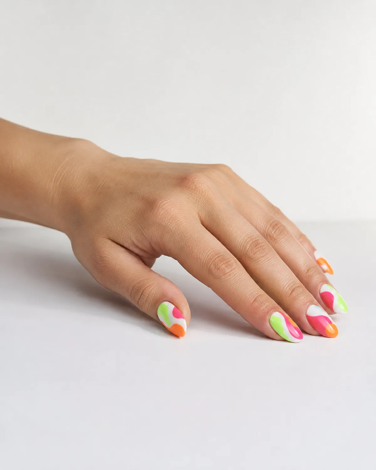 Single left hand with medium almond nails in neon pop art shapes of green pink and orange on white base on white table