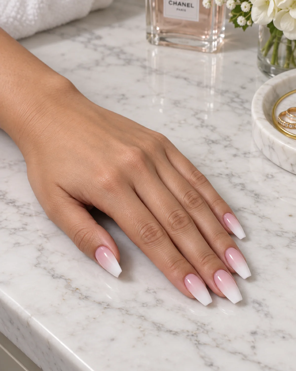 Single left hand with pink-to-white gradient polish on ballerina nails on a white marble counter