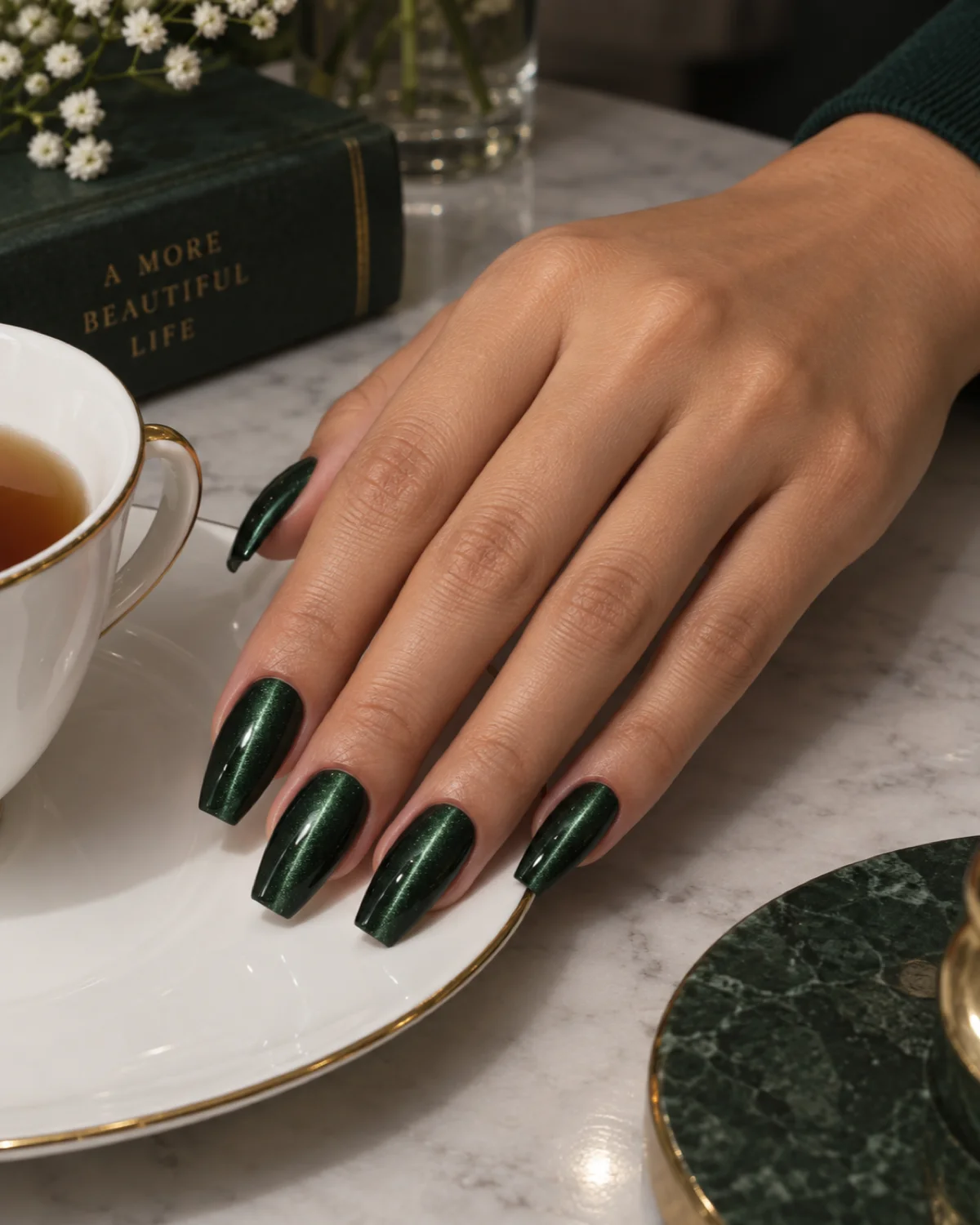 Single right hand with dark emerald cat-eye magnetic polish on ballerina nails resting on a porcelain saucer
